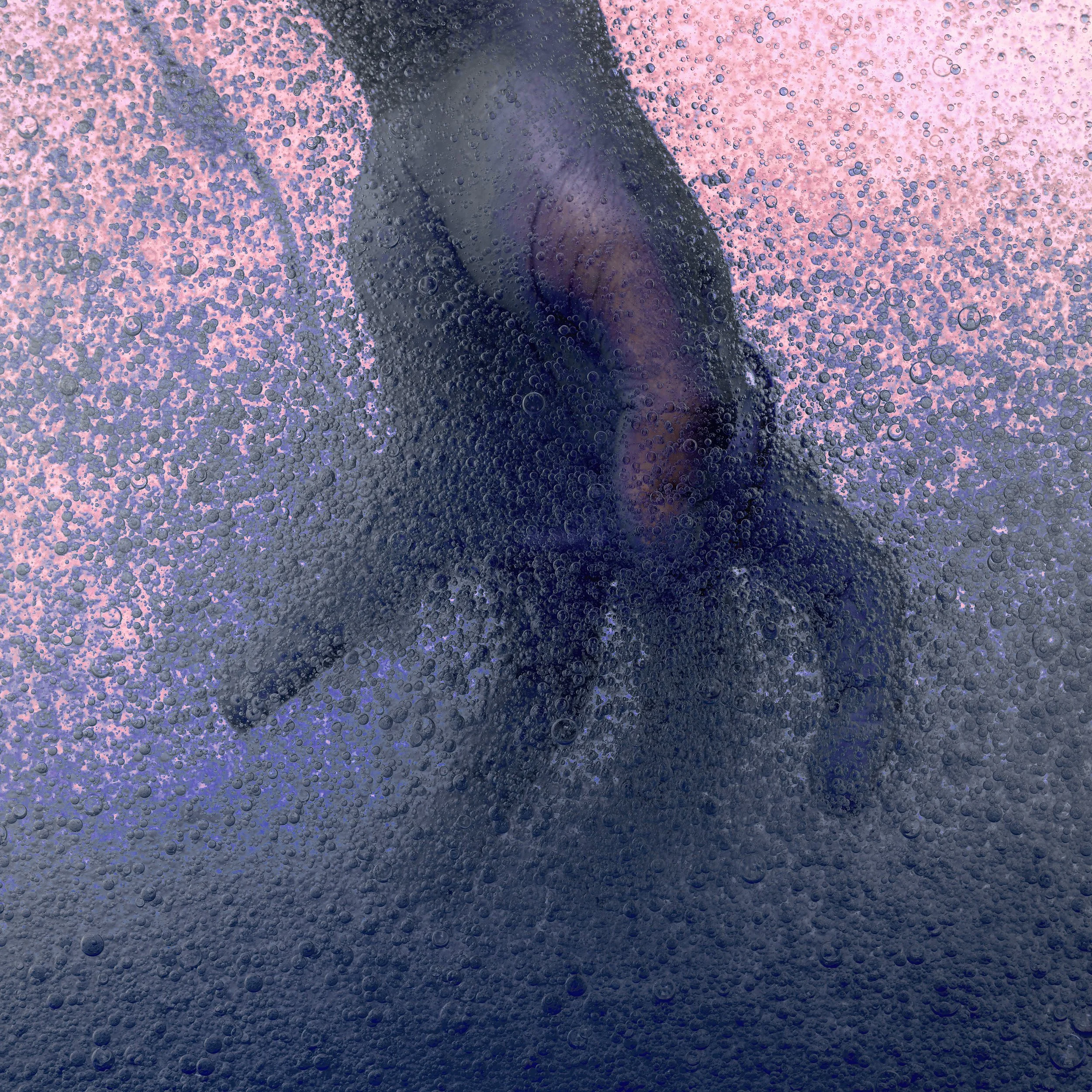 A person inside a glass with condensation and bubbles, seen through the glass with pink and purple lighting.