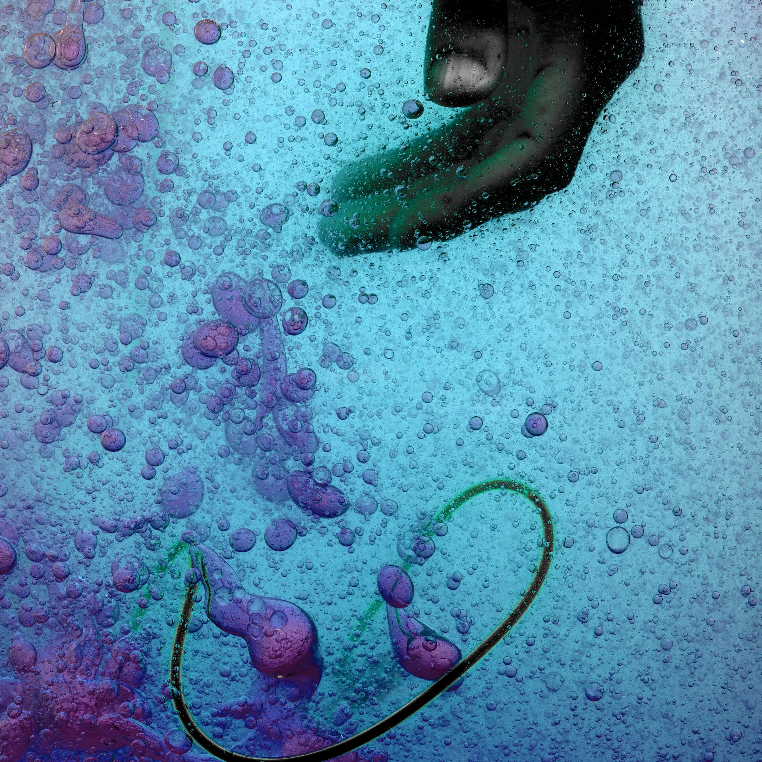 Close-up of a fishhook with purple and pink ink or dye in bubbly blue water.
