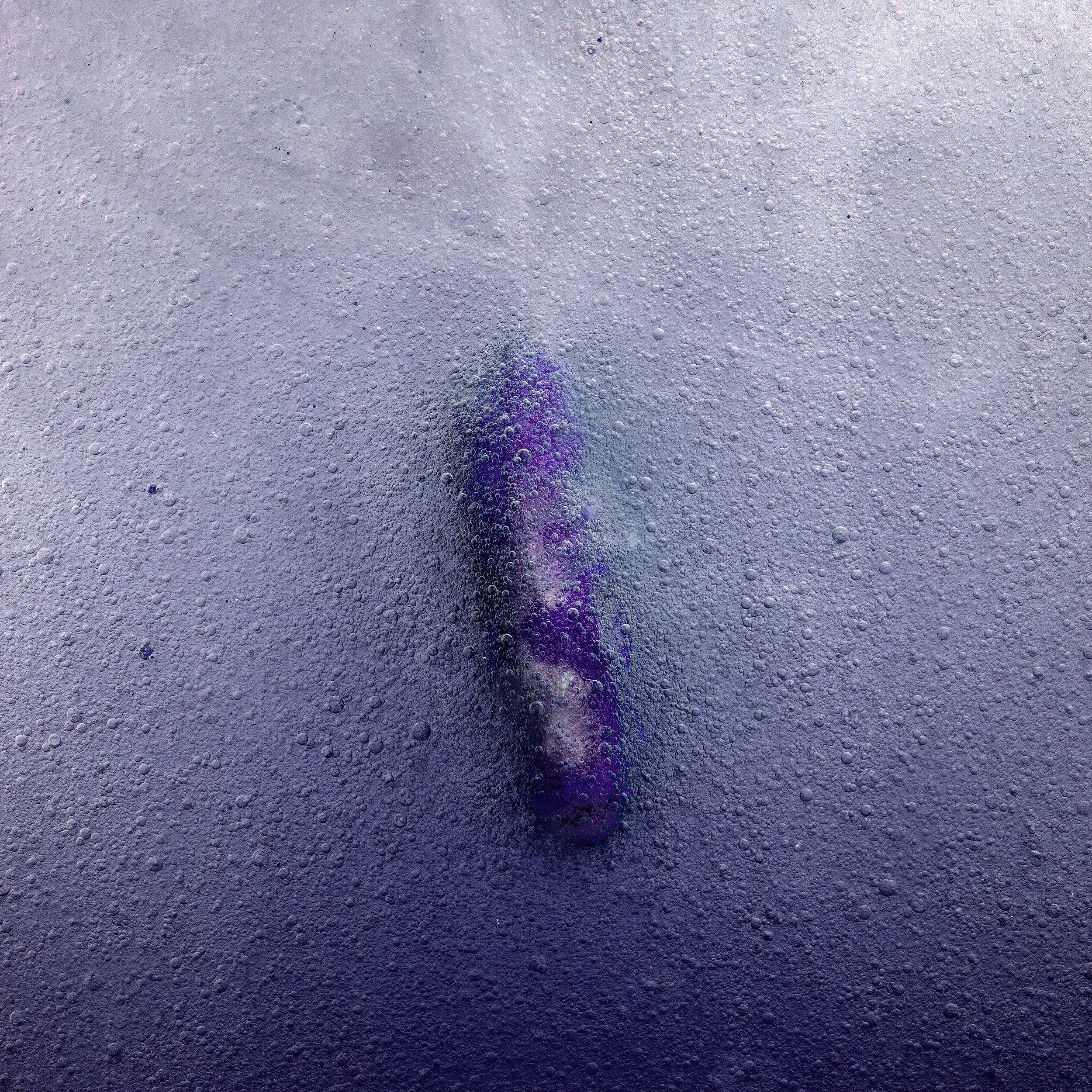 Purple and white ink swirling in dark water with bubbles surrounding it.