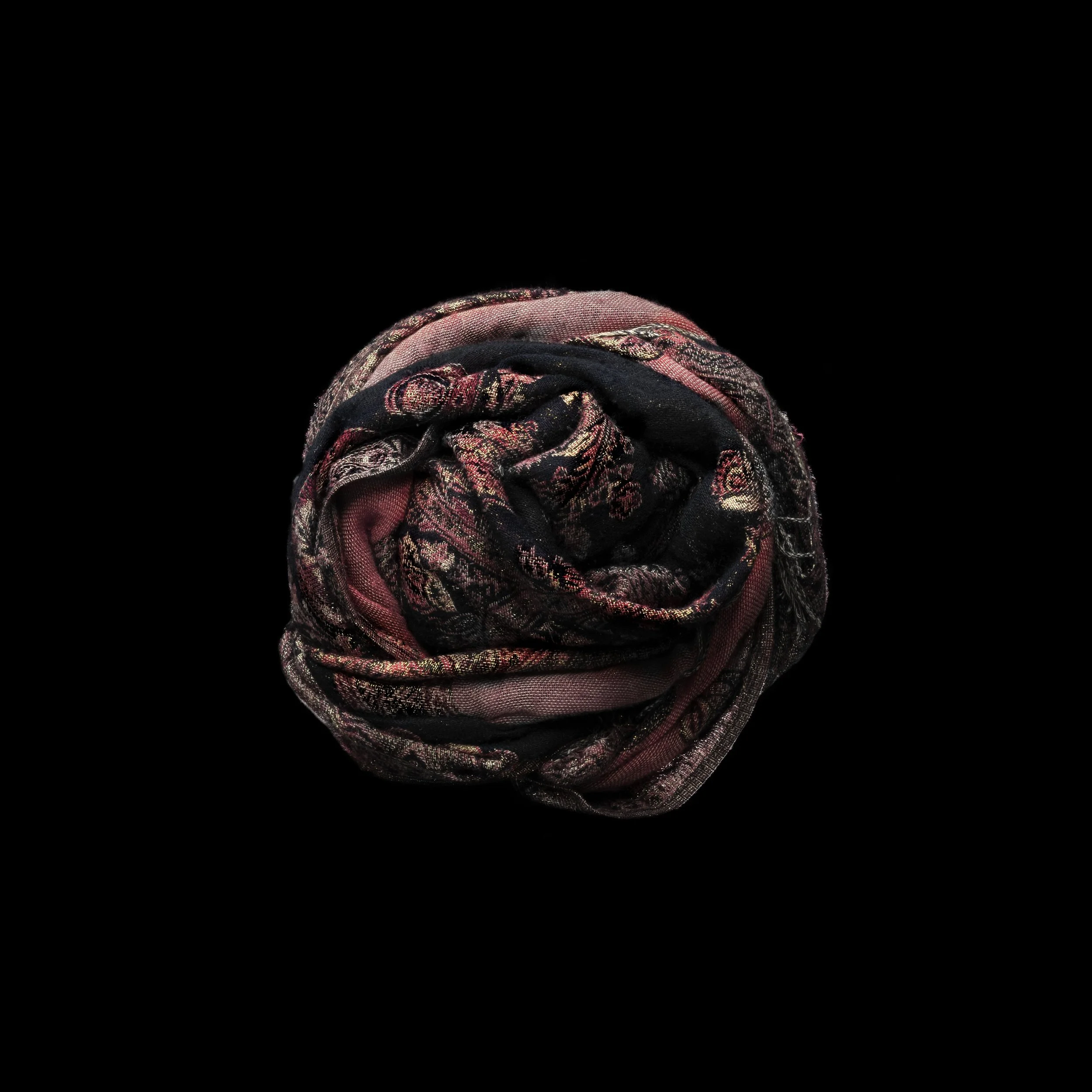 A rolled fabric with a detailed floral pattern in shades of pink and black, centered on a black background.