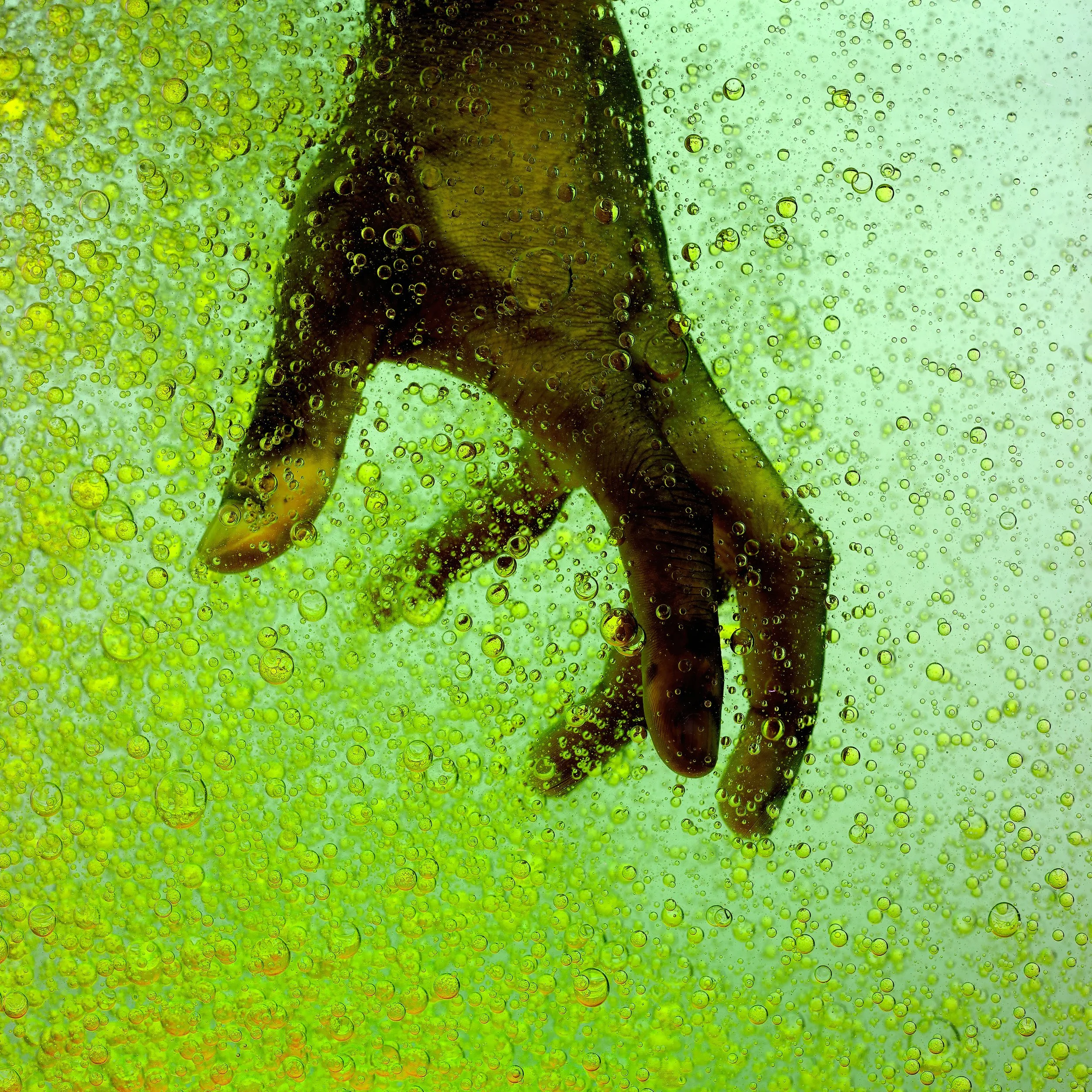 A human hand submerged in a fizzy green liquid, surrounded by numerous bubbles.