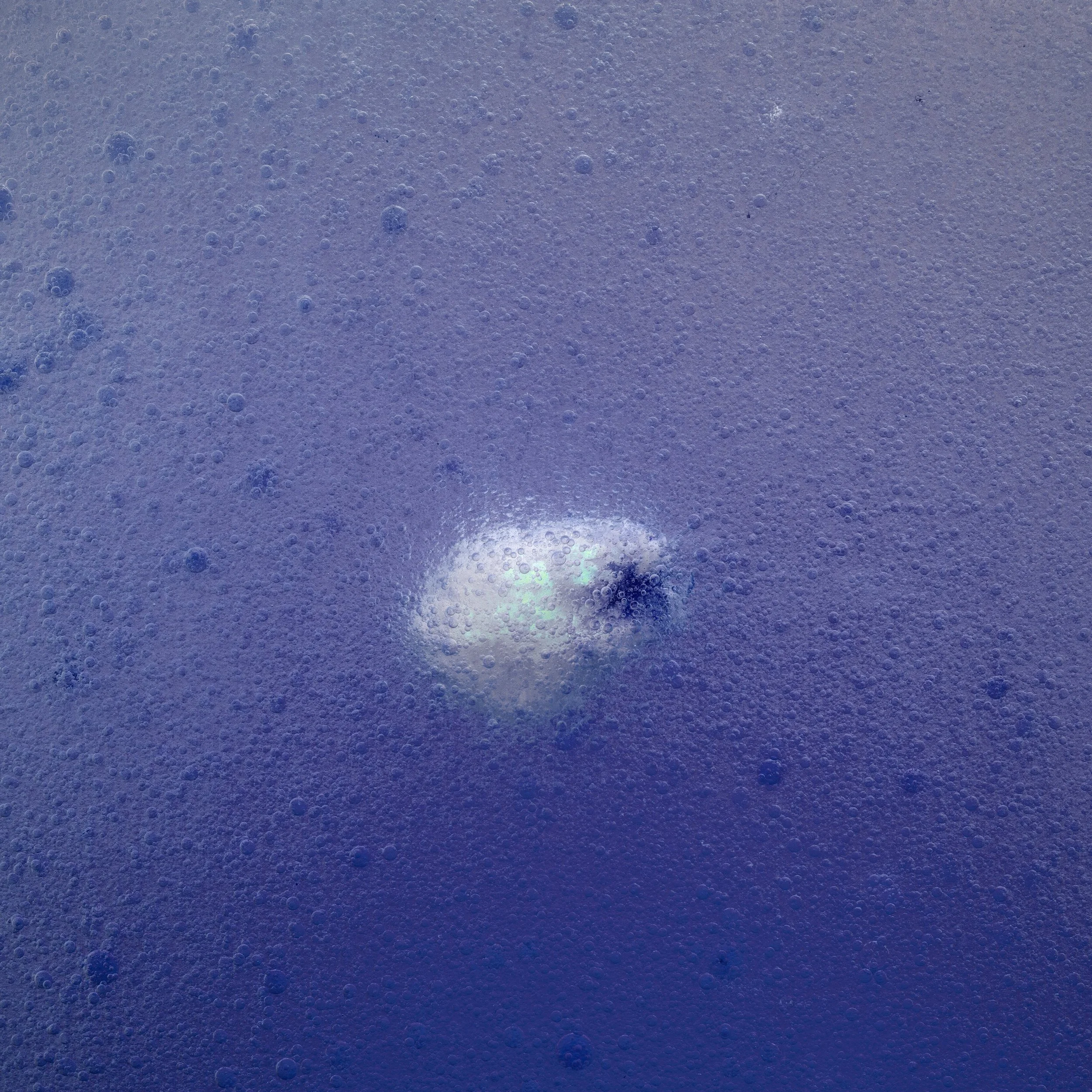 Close-up of a bubbling surface, possibly a carbonated beverage or soda, with tiny bubbles and a bright spot reflecting light.