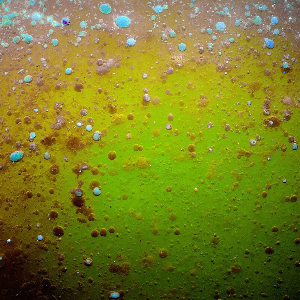 Close-up of a bubbly, foamy surface with yellow and green colors, featuring numerous small and large bubbles.
