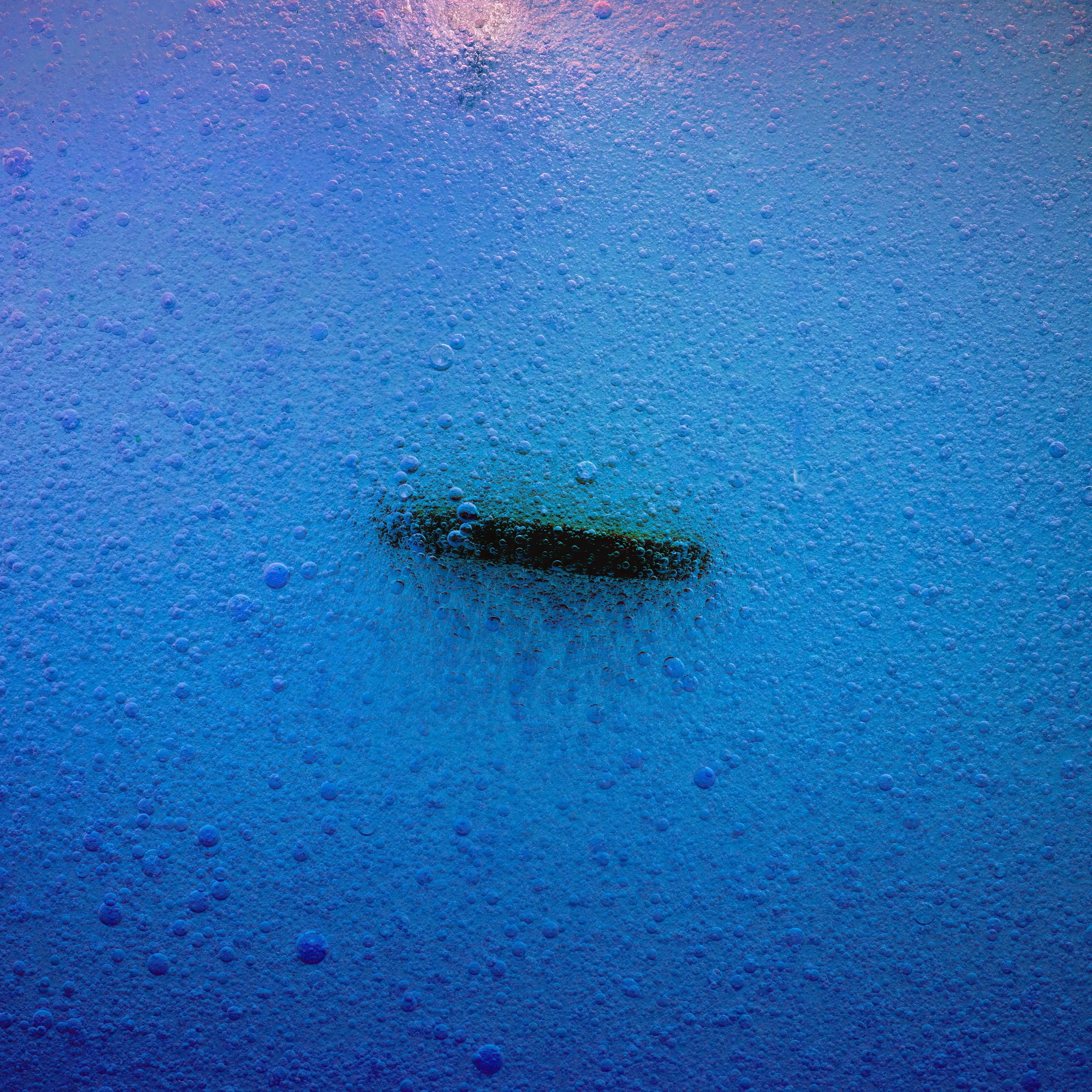 Close-up of bubbling blue liquid with a dark object submerged in the center.