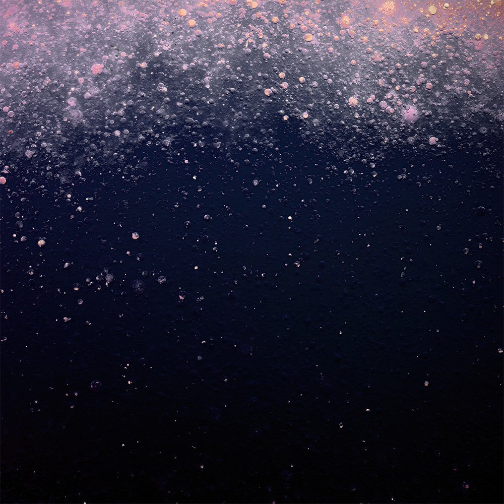Close-up of bubbles forming on a dark liquid surface, with pinkish light reflections.