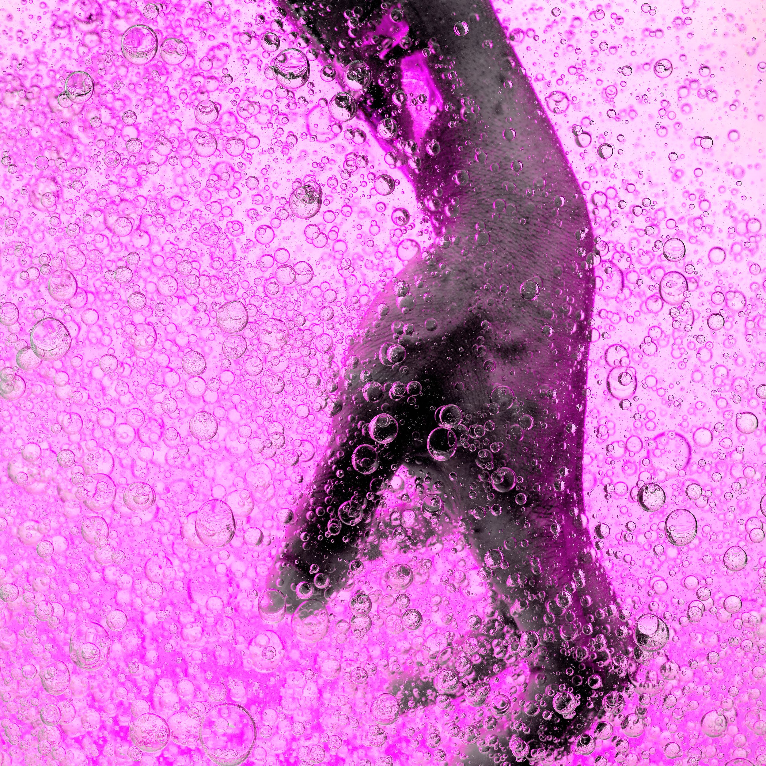 A person underwater surrounded by numerous bubbles with a pink background.