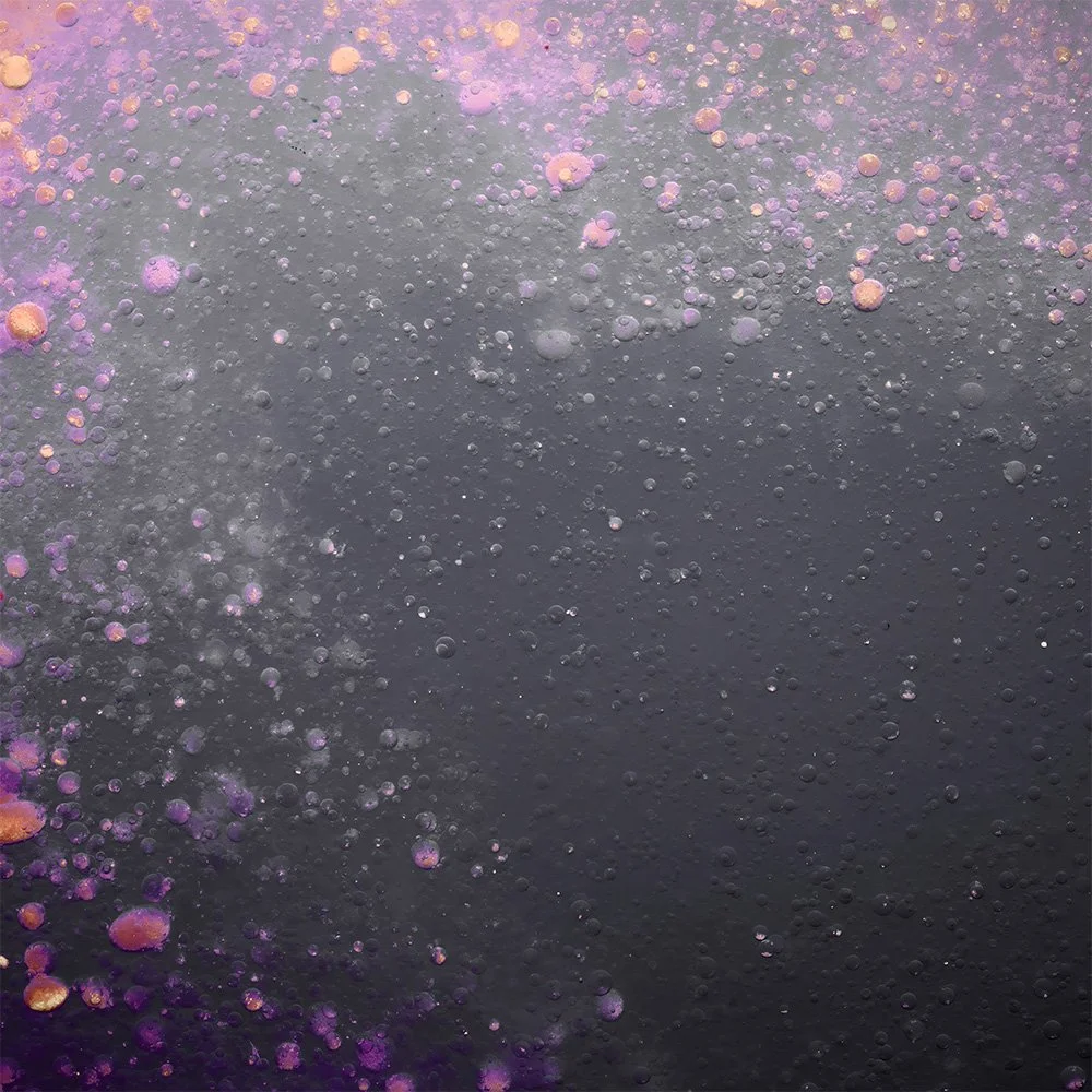 Close-up view of bubbles and foamy texture in a dark liquid, with purple and orange colors scattered throughout