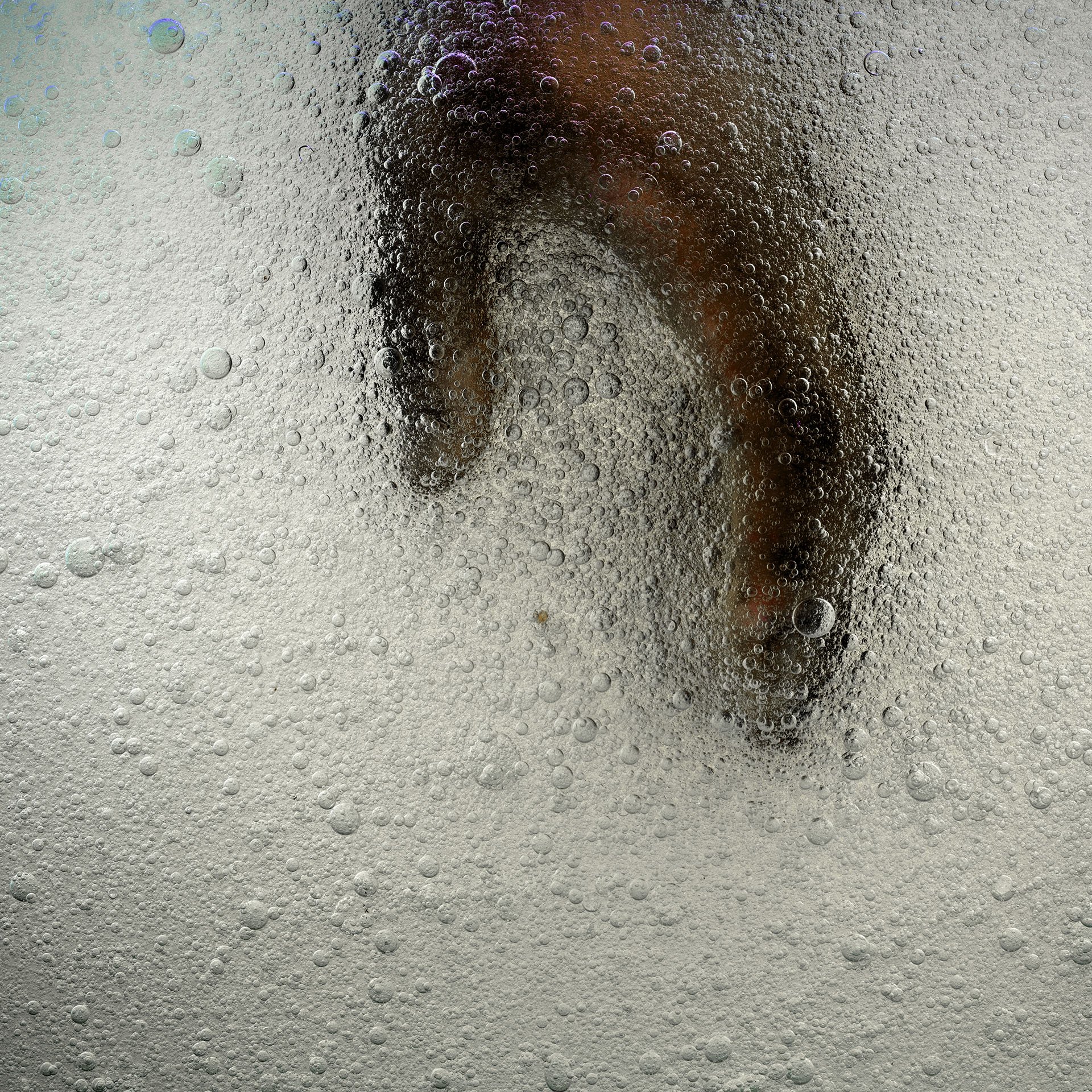A person with dark hair shows their face through the bubbles and foam of a carbonated beverage, likely a soda or beer.