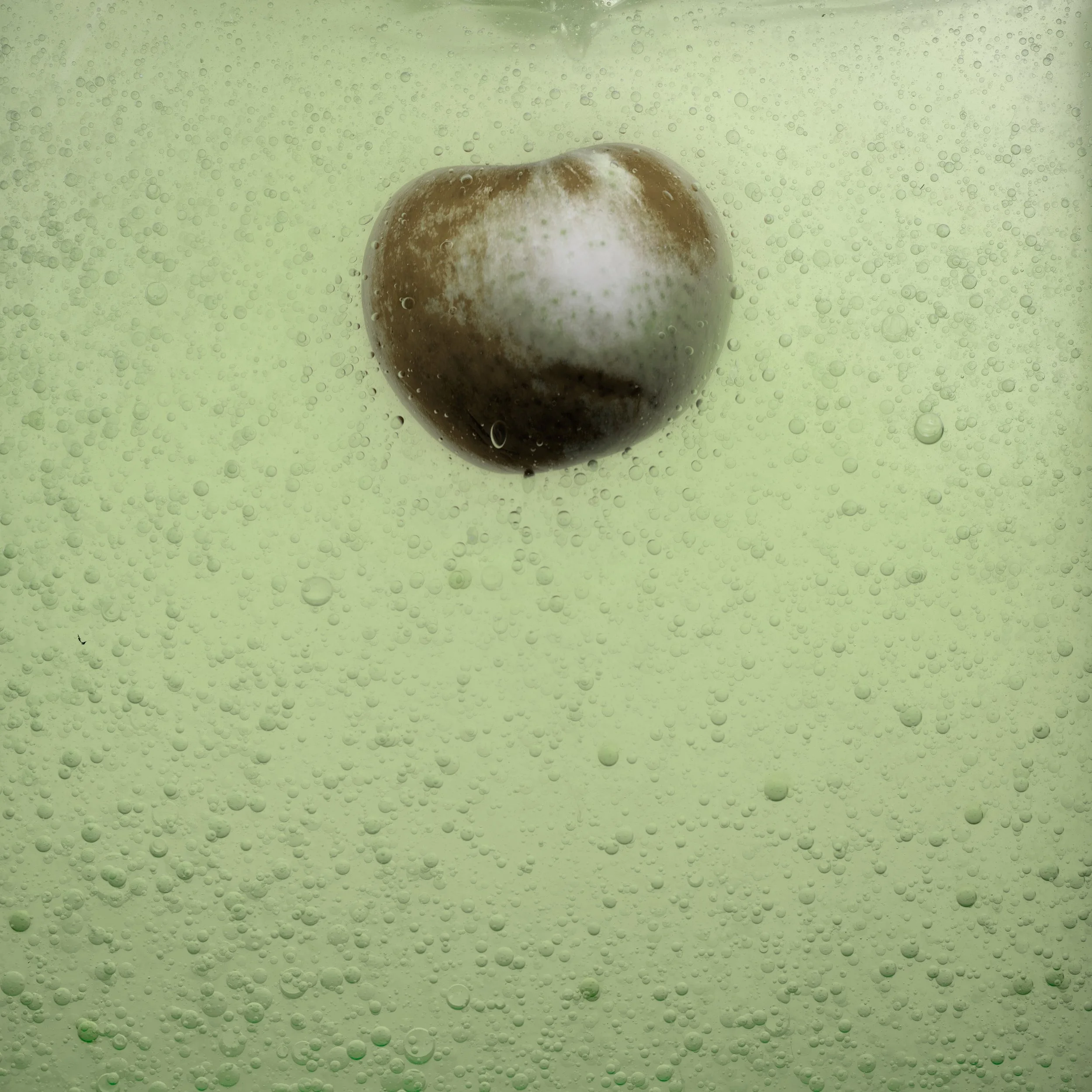 A metallic object that looks like a fruit, possibly an apple, submerged in a liquid with numerous tiny bubbles.