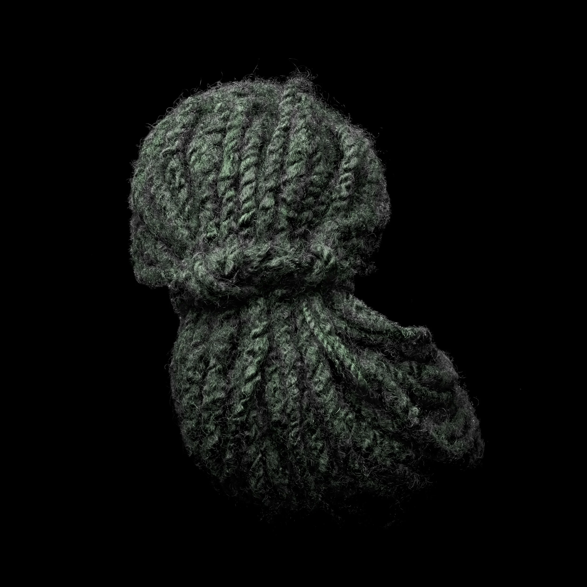 Close-up of a ball of green and black yarn with a reflection on a black background.