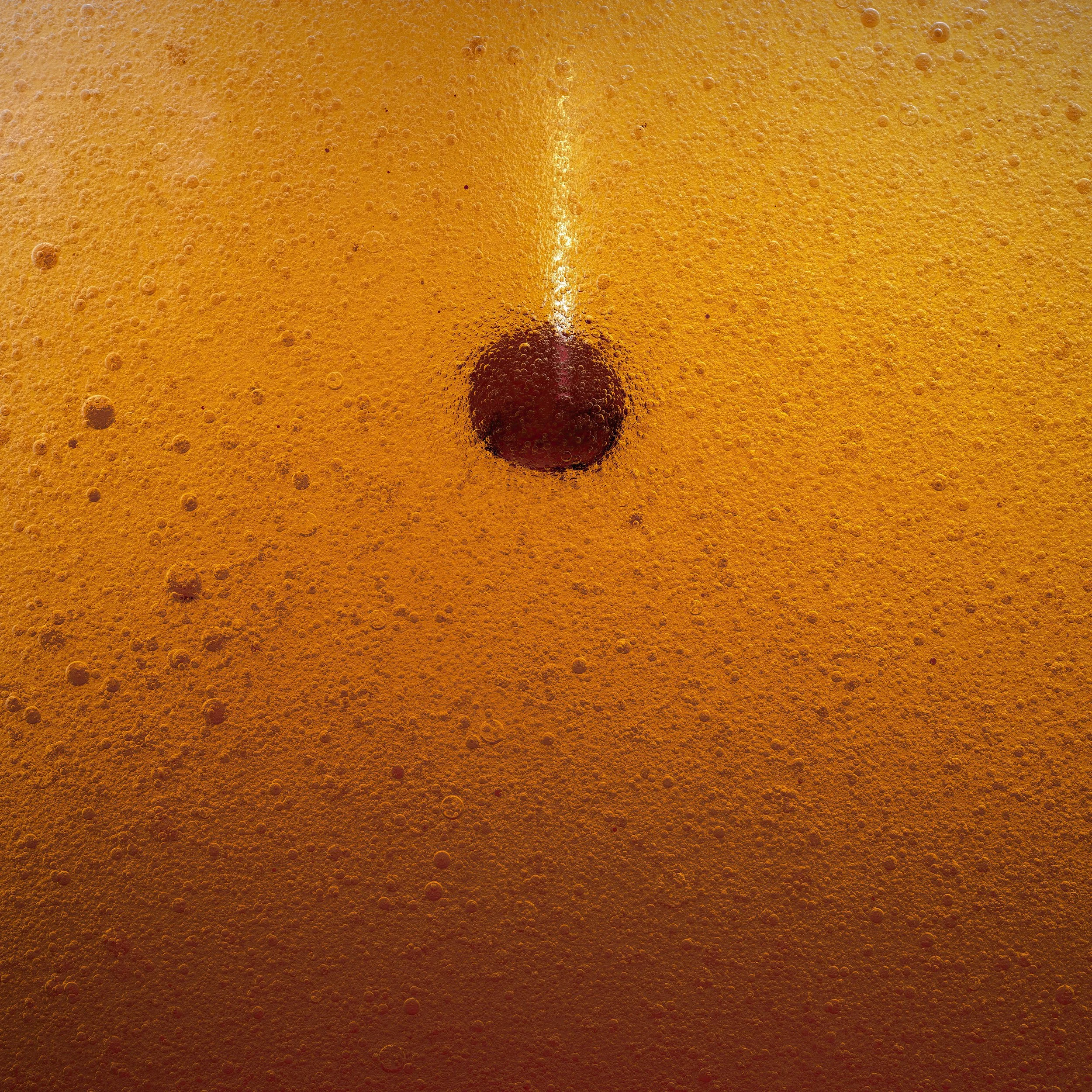 Close-up view of a cherry in a fizzy orange soda, with bubbles surrounding it and a white straw positioned above the cherry.