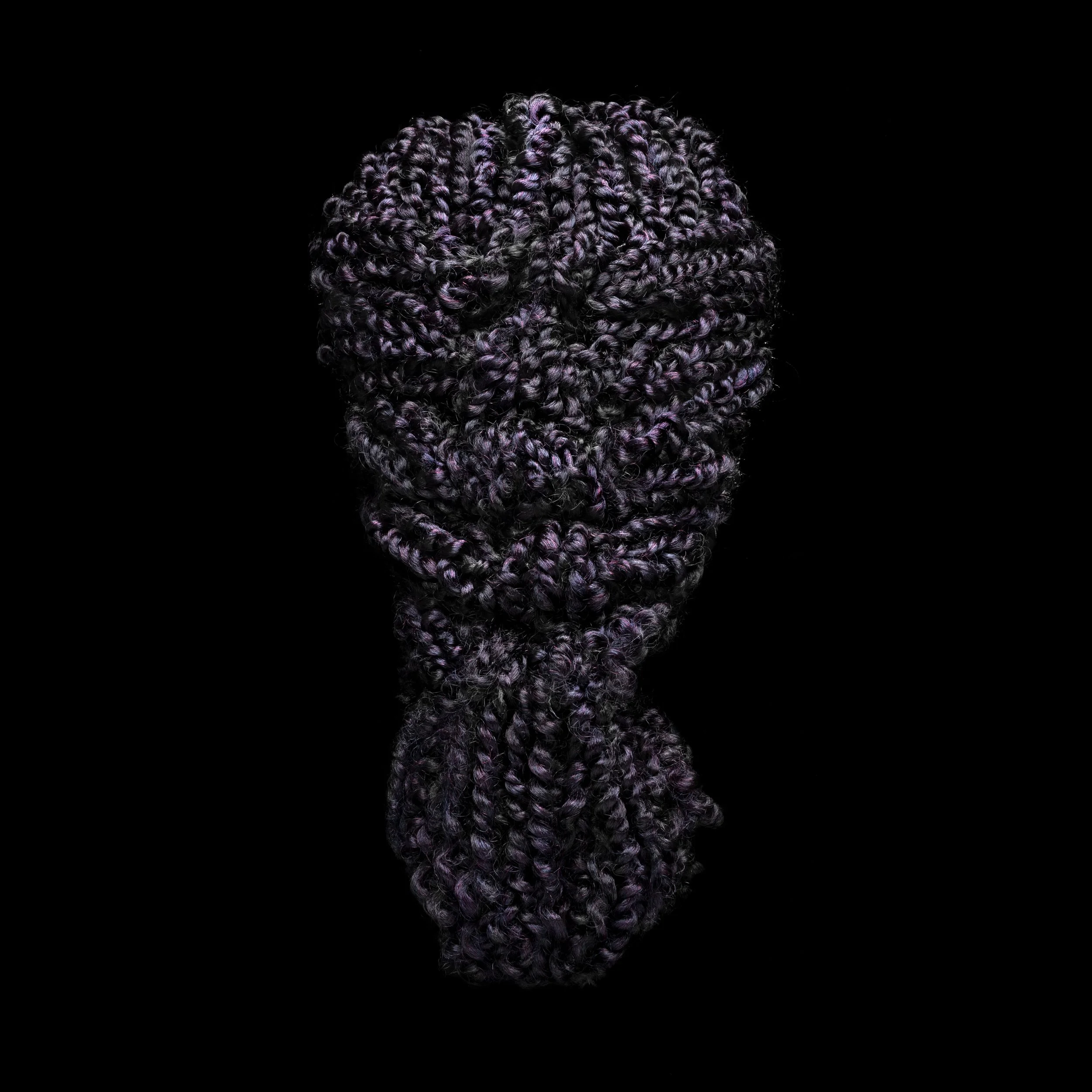 Close-up of a bundle of tightly coiled purple black hair extensions against a black background.