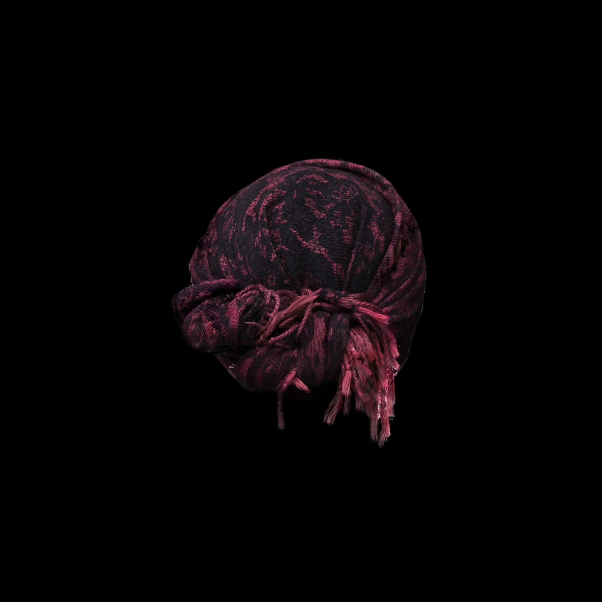 A black and pink patterned headscarf tied in a knot, centered against a black background.