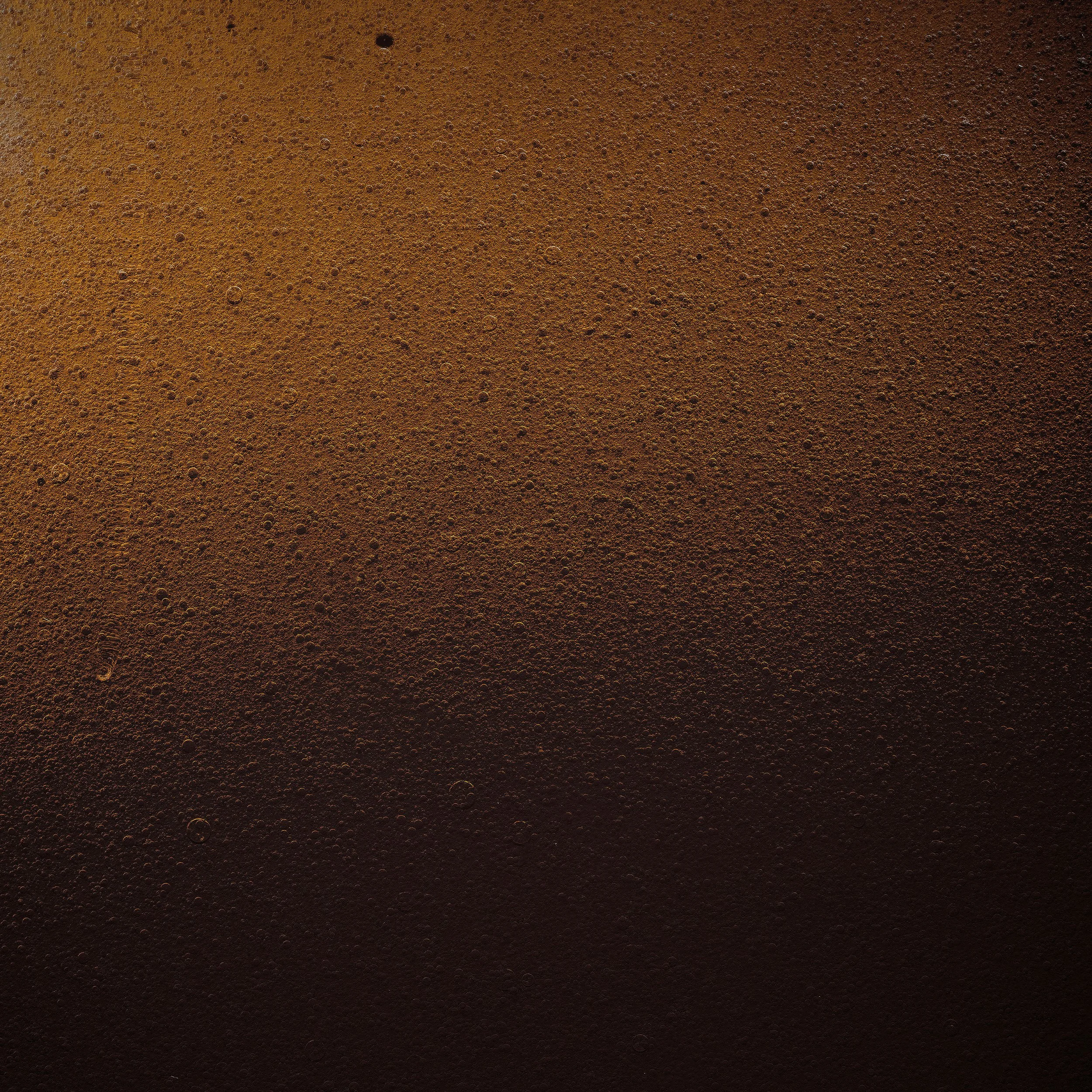 Close-up of the surface of a dark brown beverage with bubbles, likely a beer.