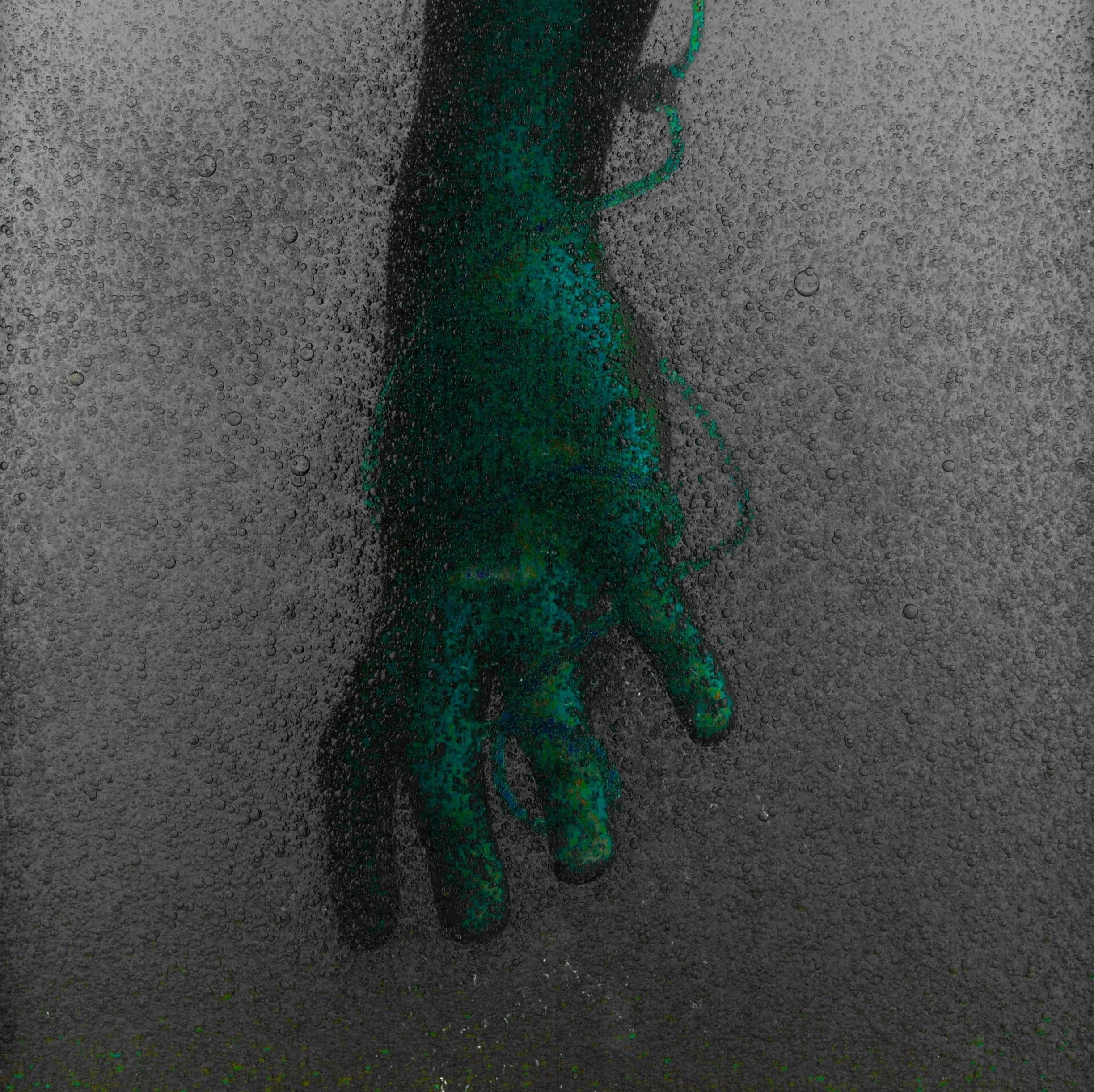 Close-up of a hand pressing against a glass surface with water droplets and bubbles on it.