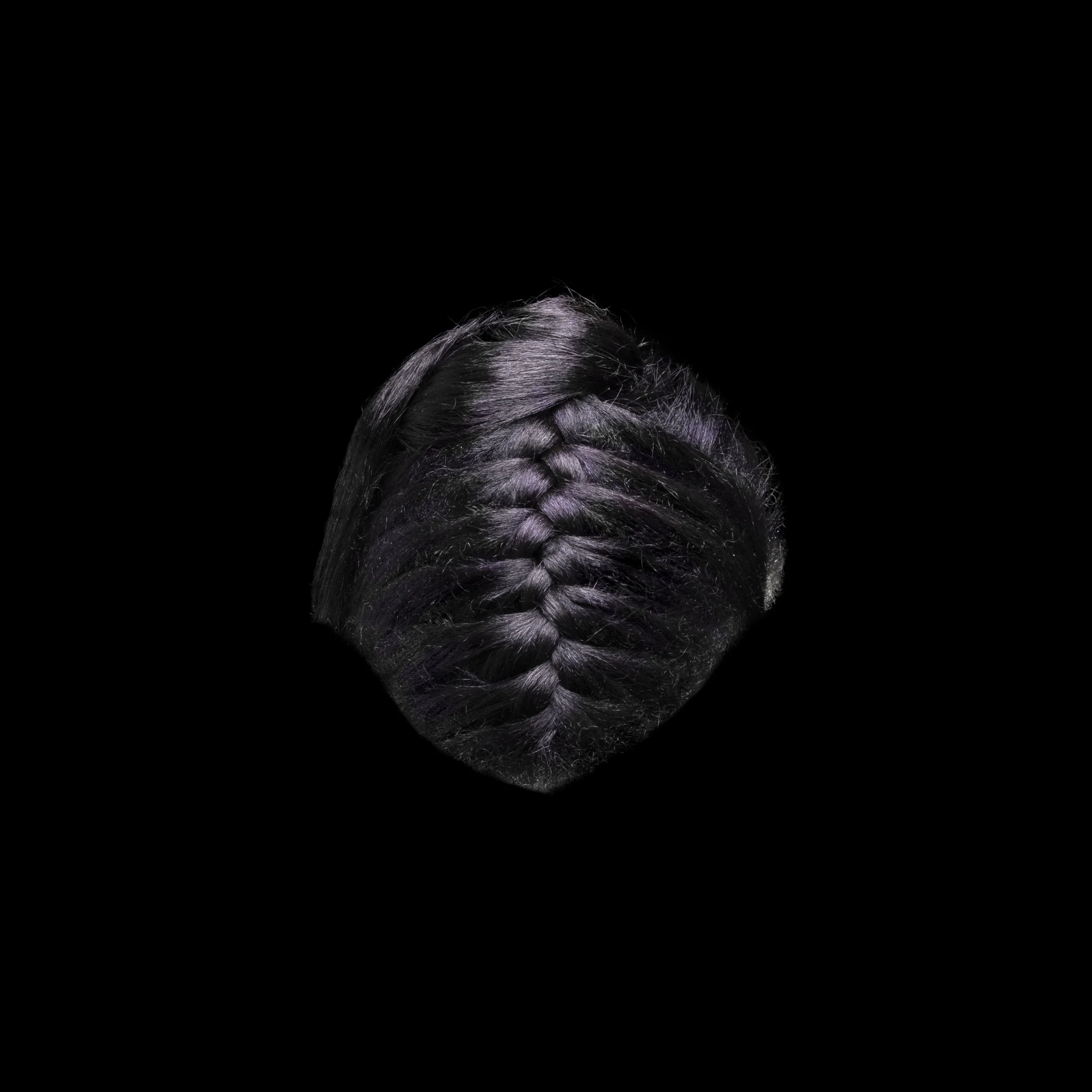 Close-up of a person's head with black hair styled in a French braid on a black background.