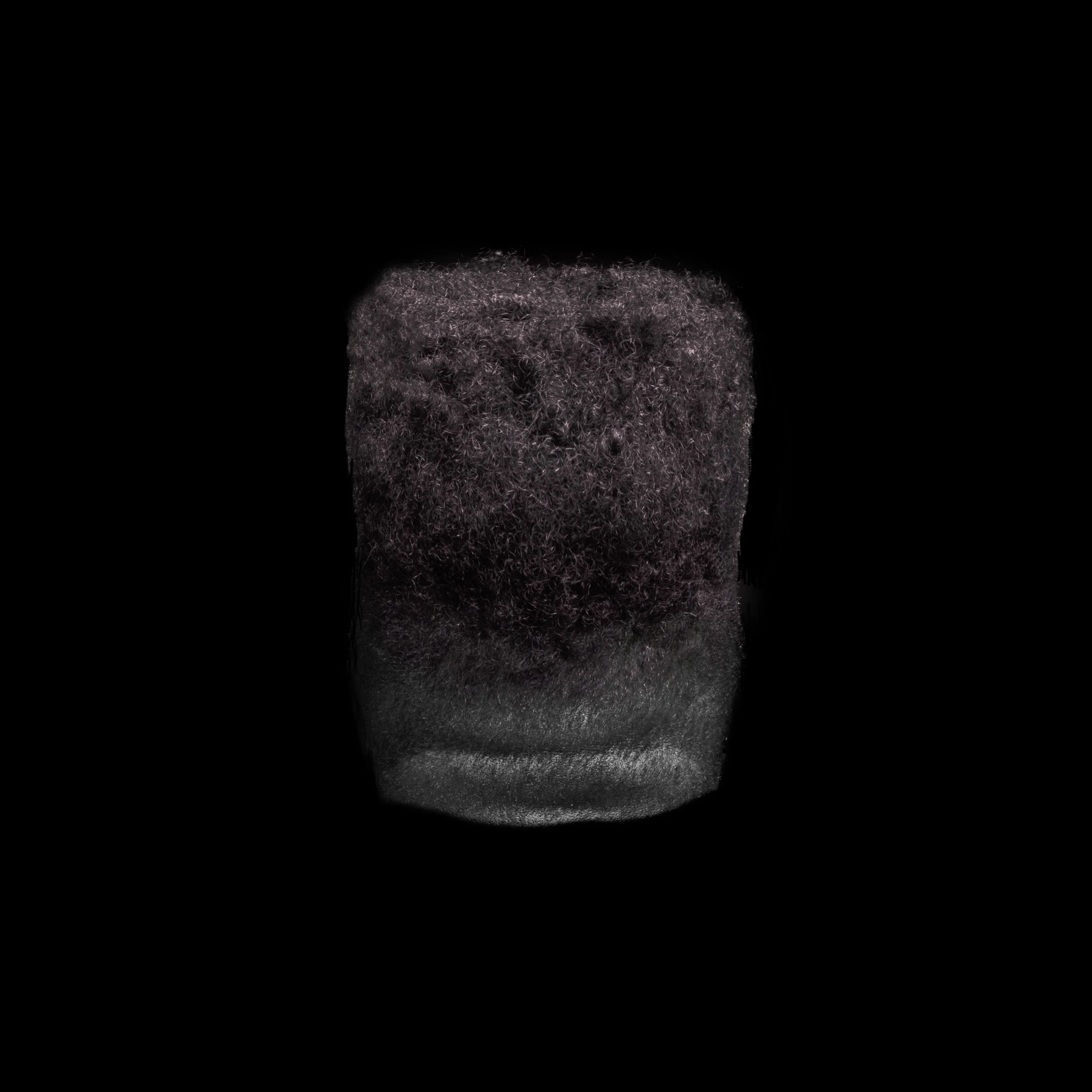 A close-up of a black, fuzzy, textured object resembling a synthetic or natural fiber above a dark gray base on a black background.