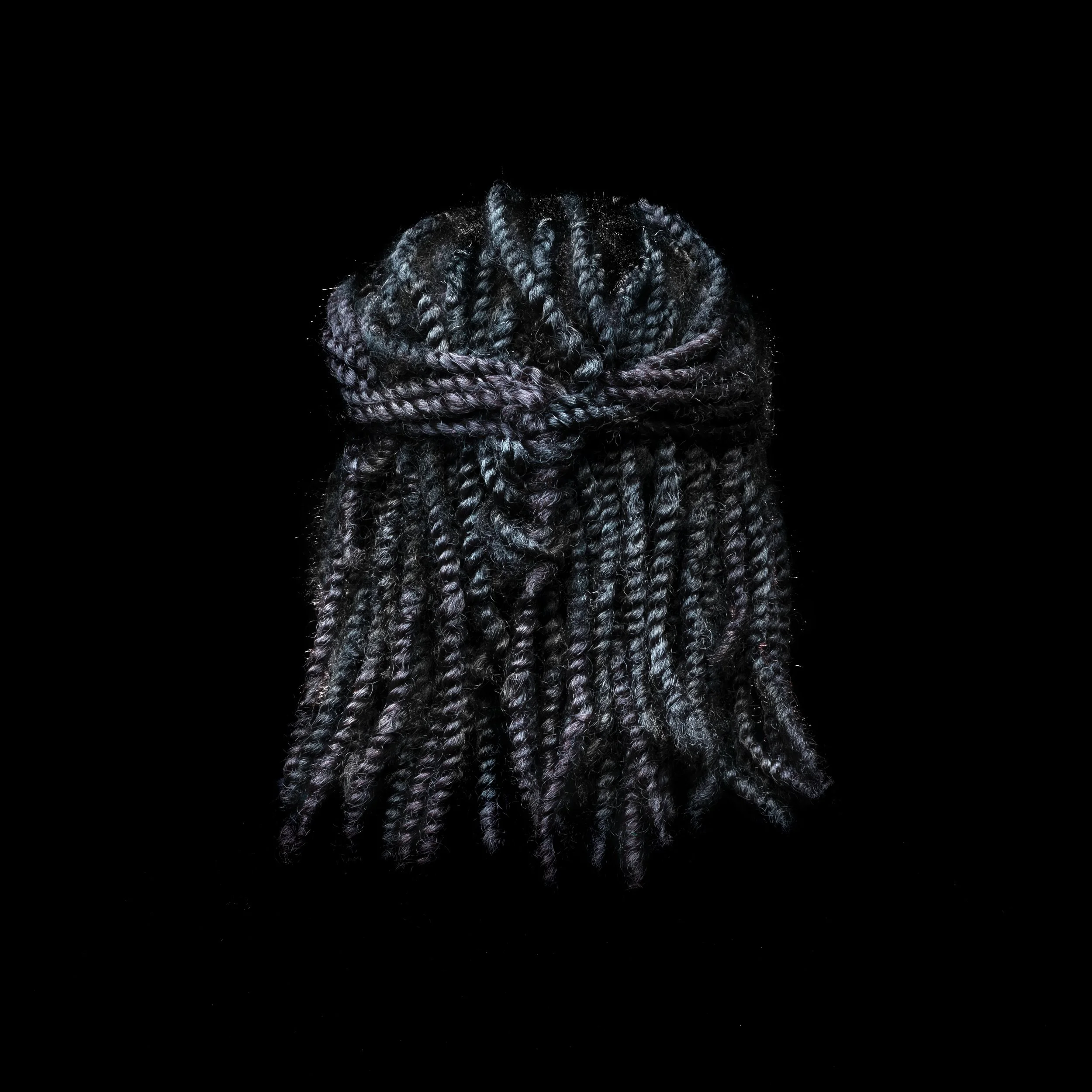 Back view of dark gray and purple braided hair against a black background.