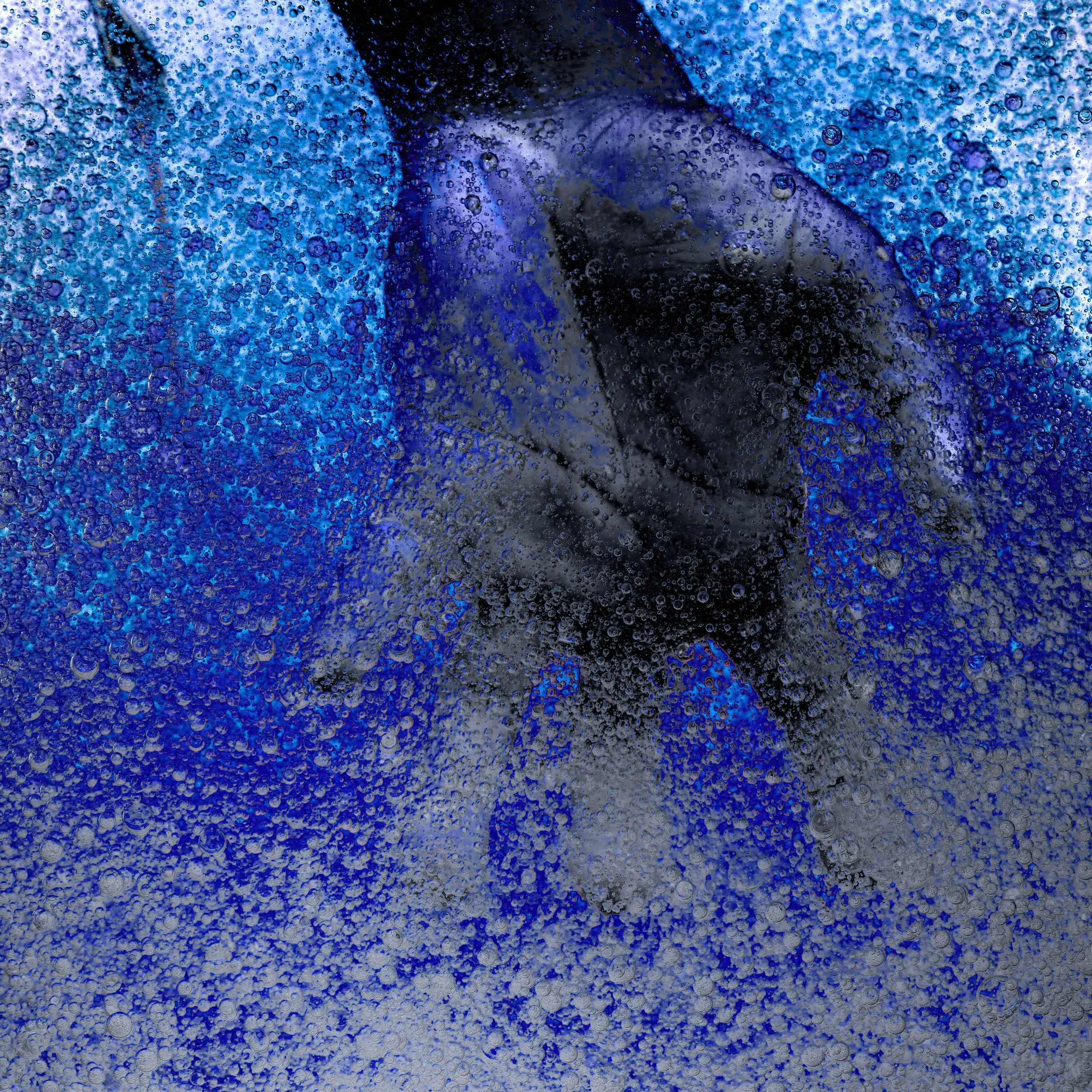 A close-up of a person inside a glass with bubbles, wearing a dark jacket and gloves, with a blue background.