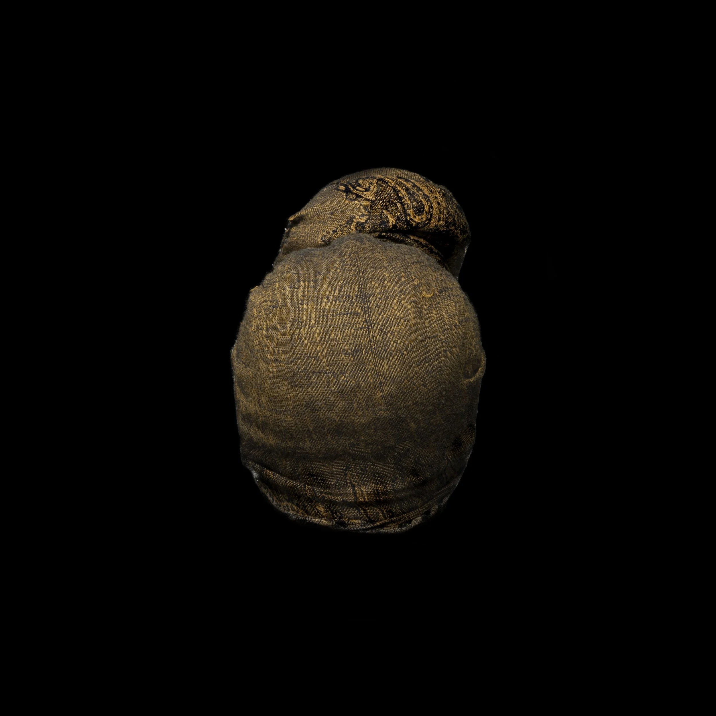 A worn, rolled fabric-covered object resembling a handmade doll or sculpture, set against a black background.