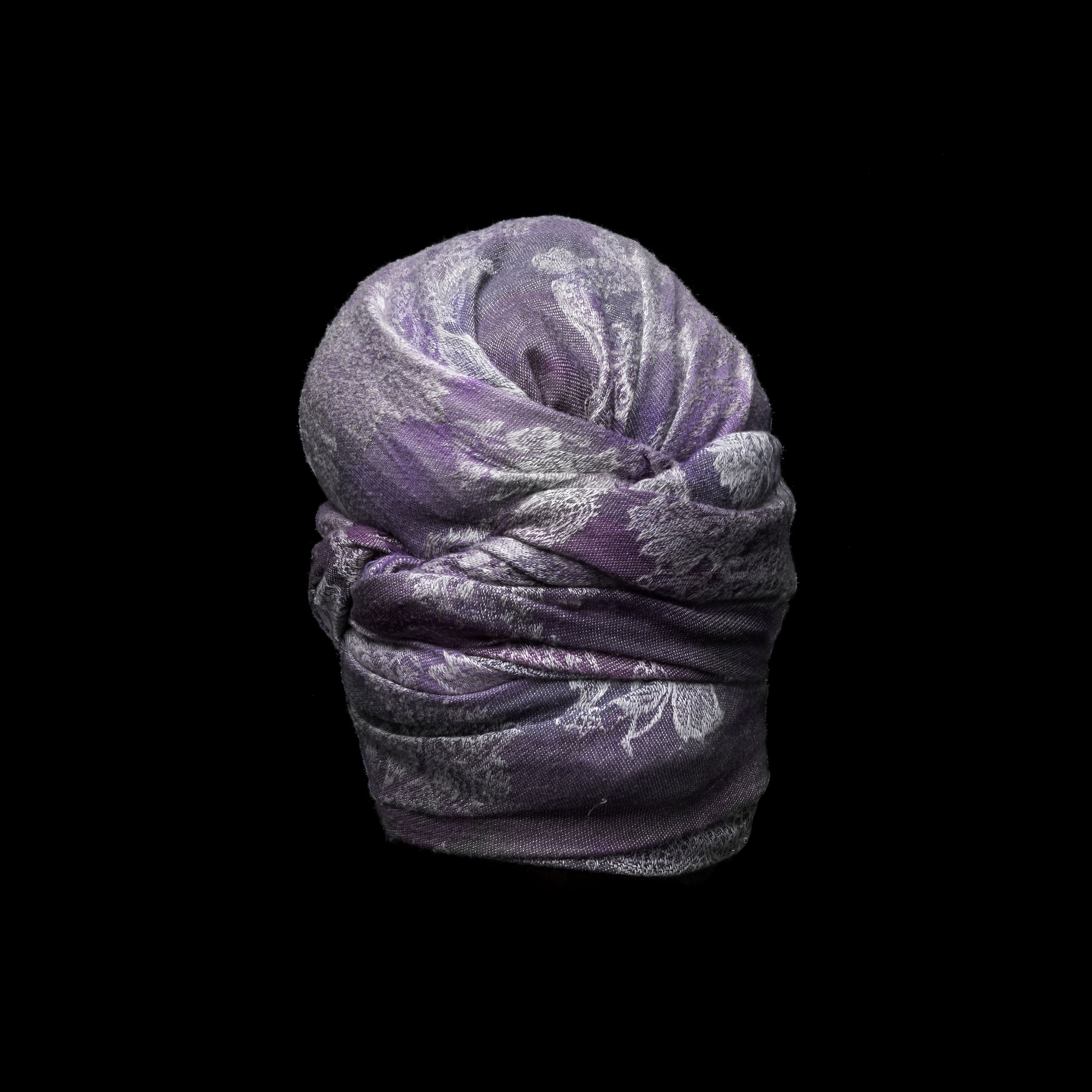 A fabric headwrap with purple and silver floral pattern on a black background.