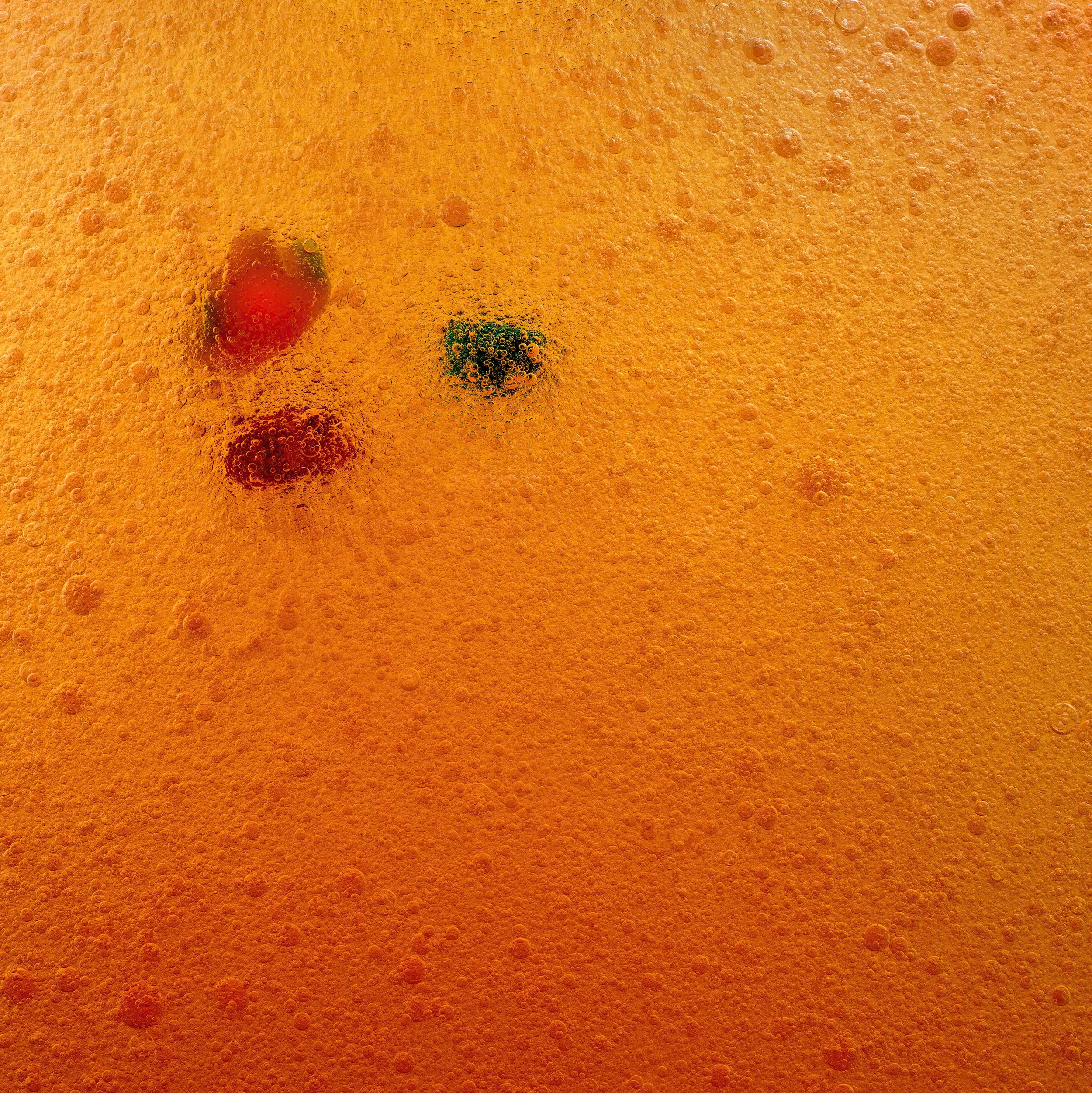 Close-up image of orange drink with bubbles and small pieces of fruit, possibly berries, submerged in the liquid.