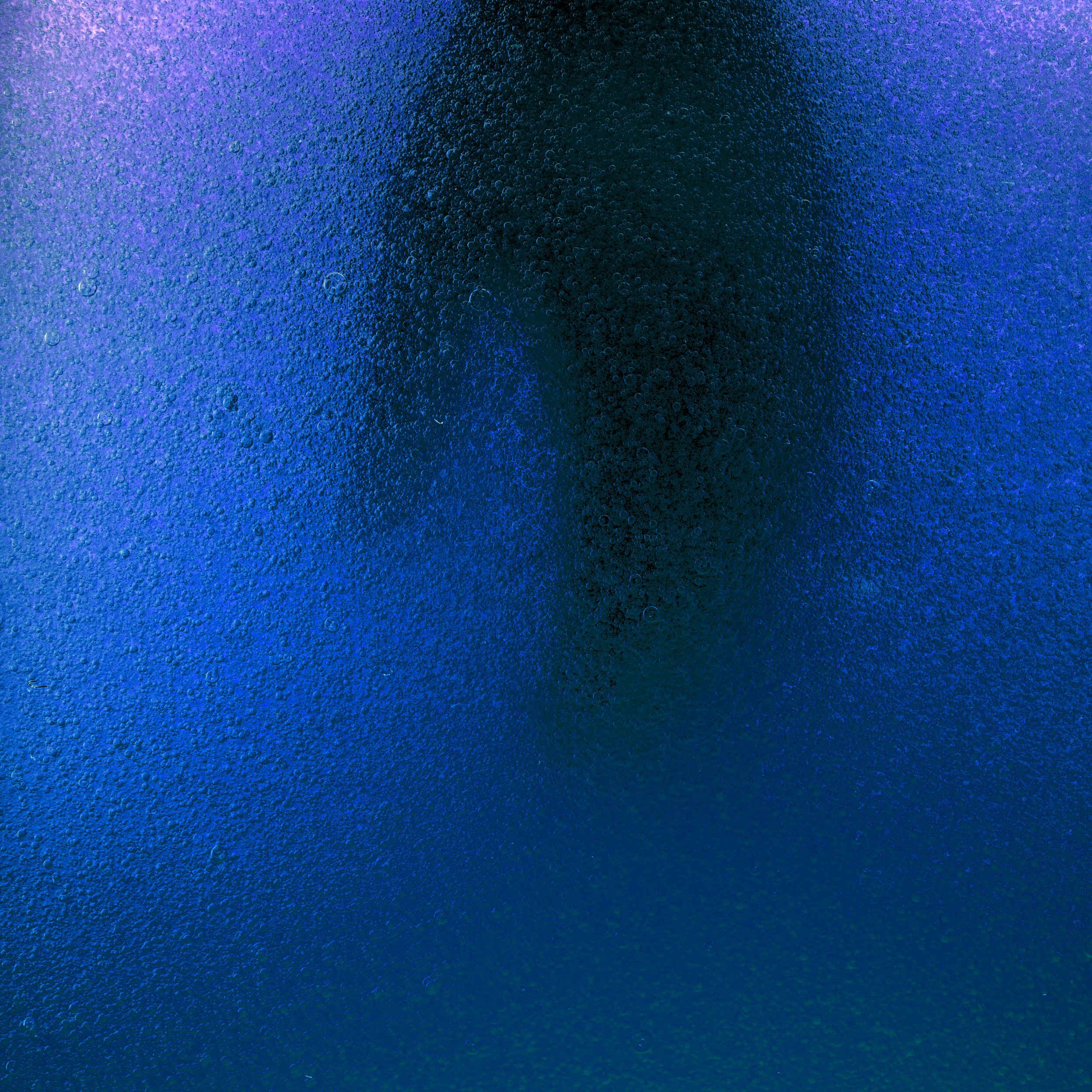 Close-up of a textured surface with a gradient of blue and purple hues, featuring tiny bubbles or particles.