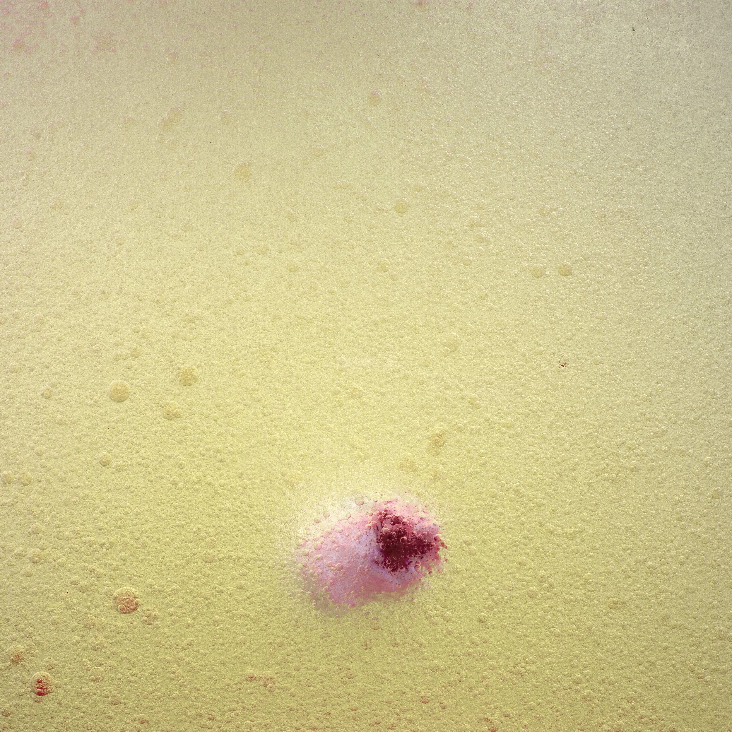 Close-up of a fizzy, carbonated beverage with a pink and red cherry in the foam.