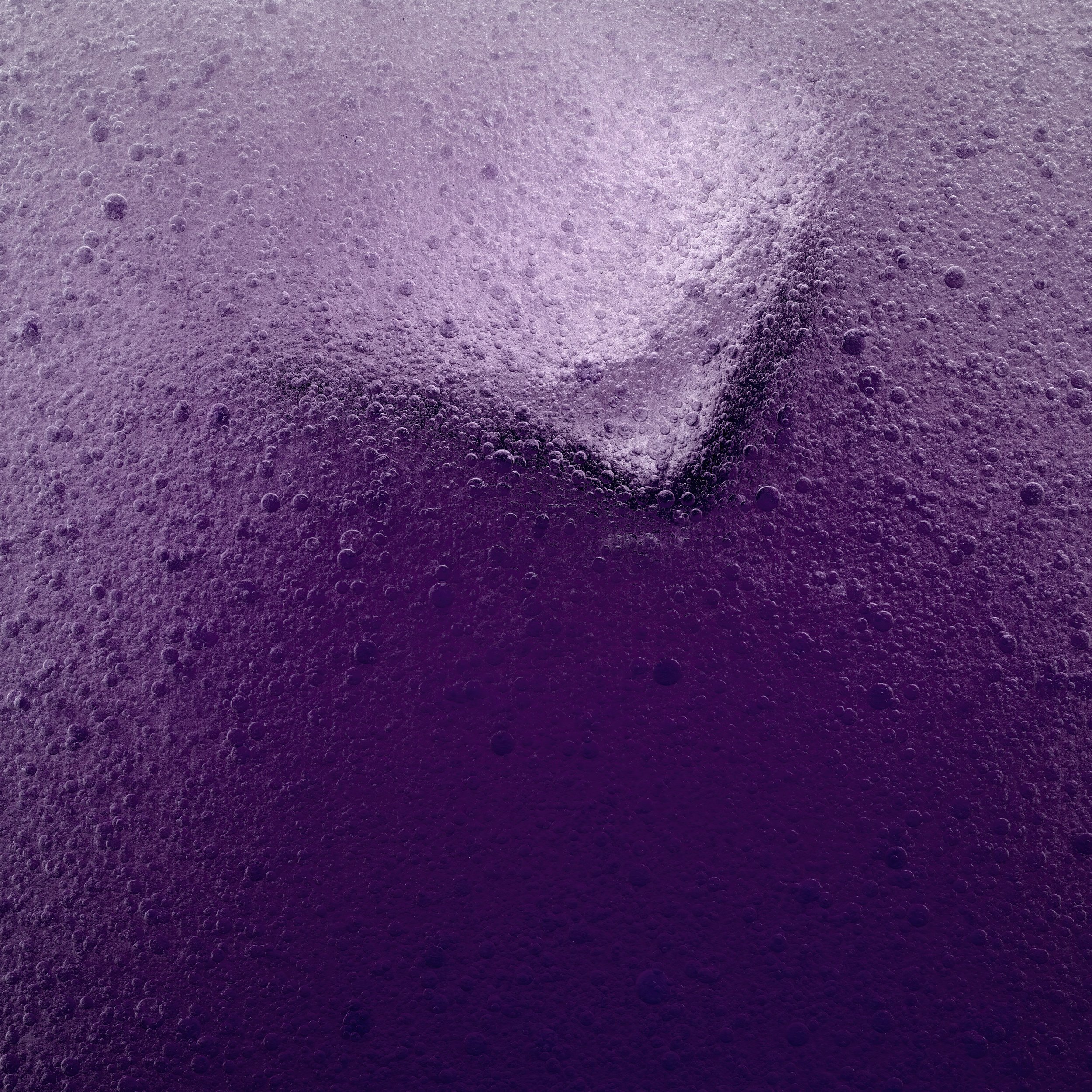 Close-up of a fizzy, dark purple beverage with a large ice cube.