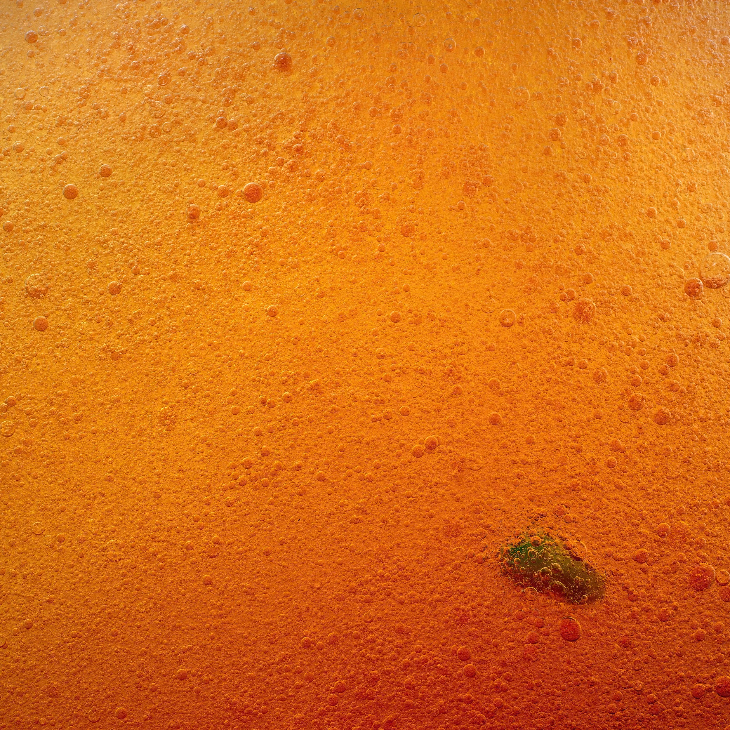 Close-up of an orange-colored beverage with bubbles and a small green leaf at the bottom.