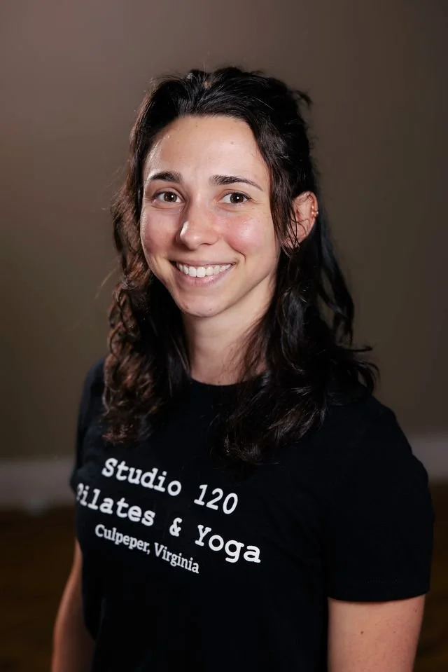 A woman smiling, wearing a black T-shirt with white text that reads 'Studio 120 Pilates & Yoga Culpeper, Virginia'.