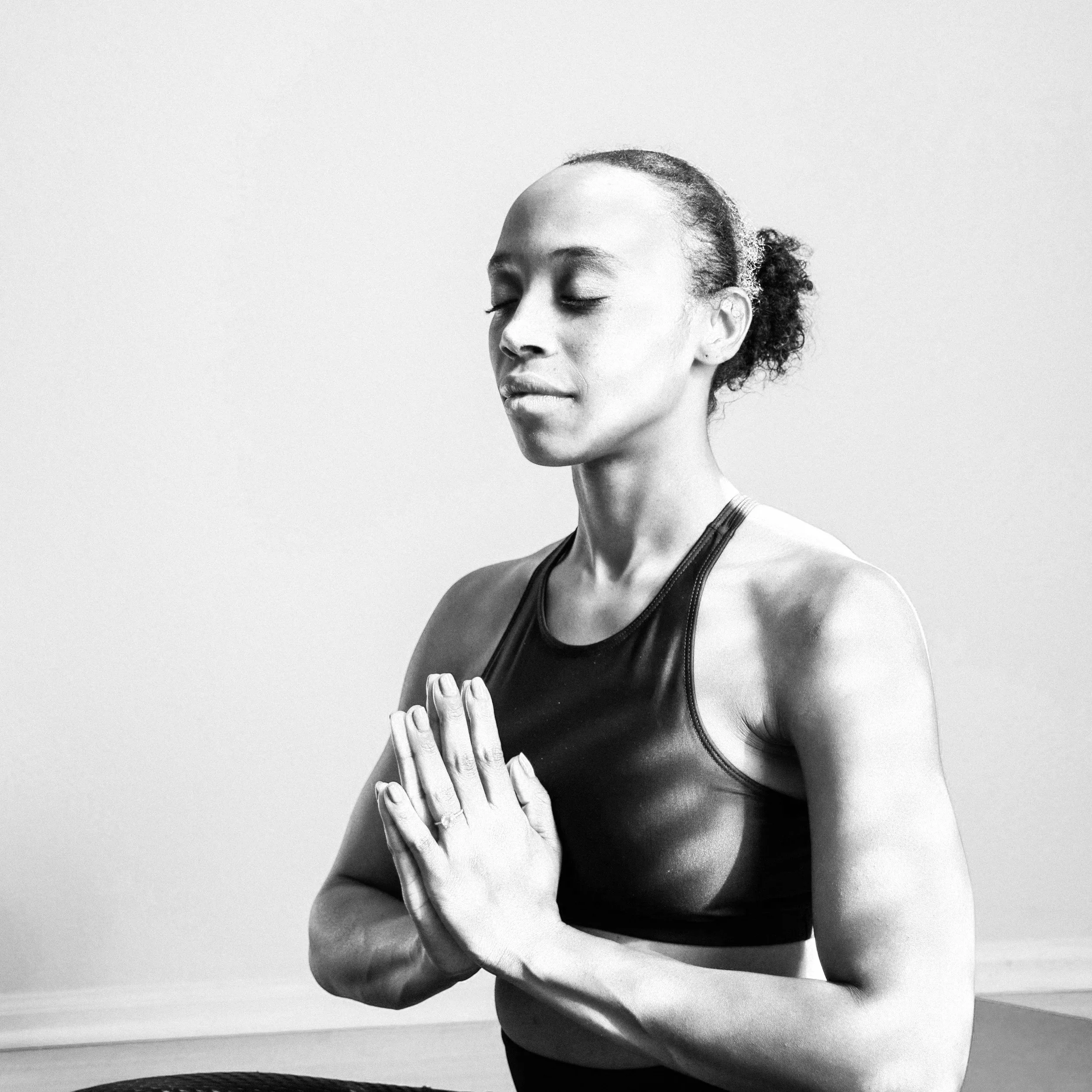 A woman practicing yoga with her hands pressed together in a prayer position, eyes closed, in a peaceful state.