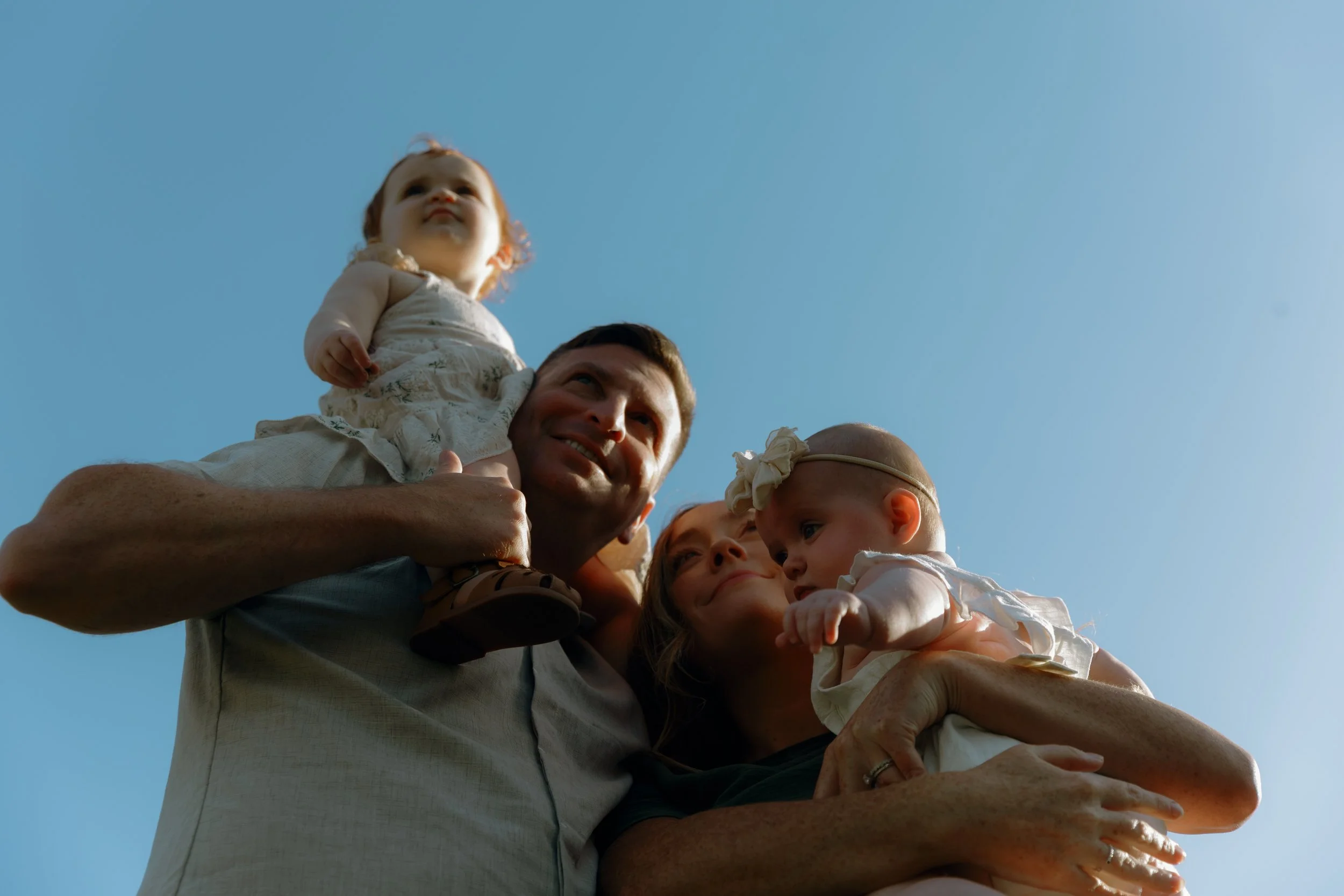 Family cuddling together while holding their toddlers up toward the sky during a golden hour family session in McHenry County, Illinois.