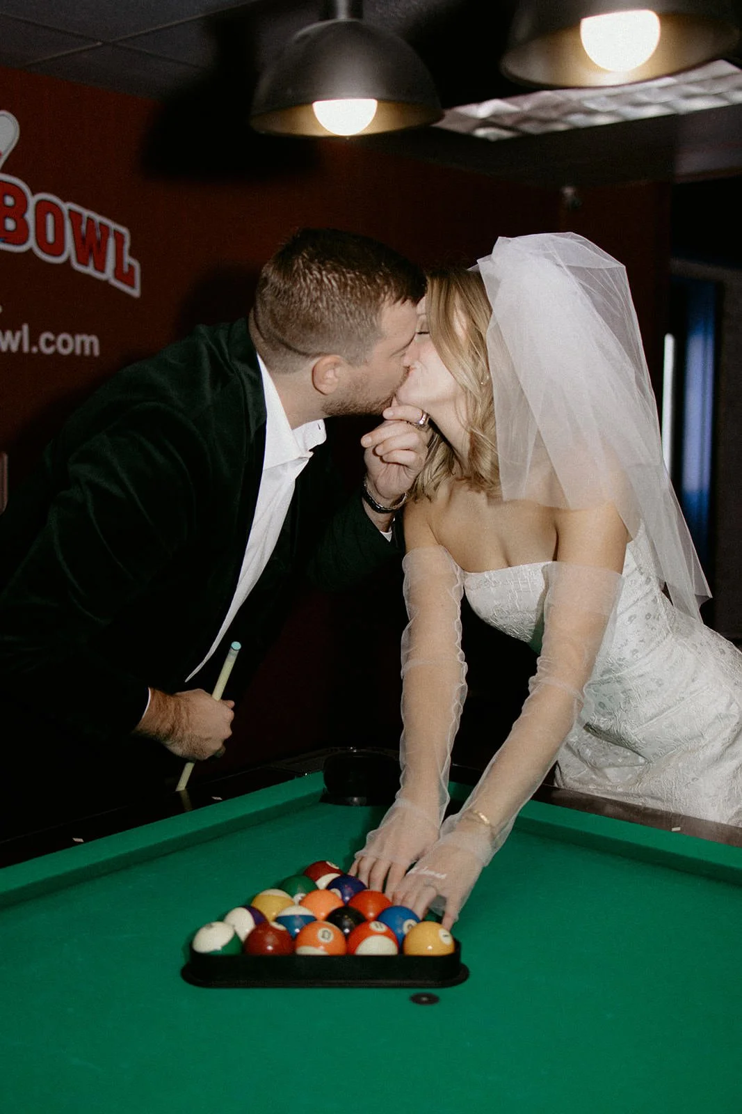 Megan and Cullen leaning over a pool table for a kiss during their retro bowling date engagement session in McHenry, Illinois.