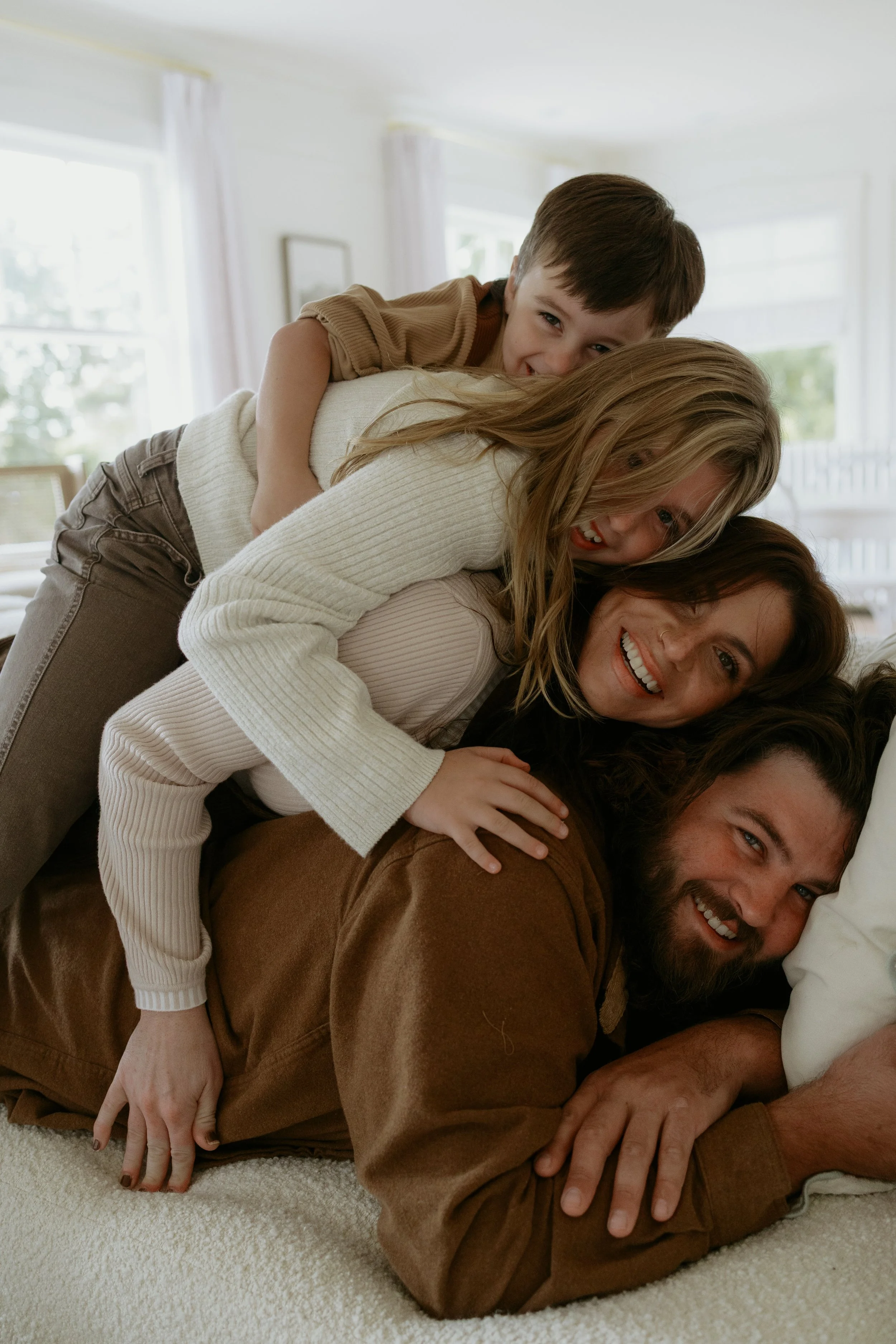 A family of four sitting on a beige couch in a brightly lit studio at The Ellery in Crystal Lake IL during their newborn family photo session indoors in the fall with Nicole Kilday Photography