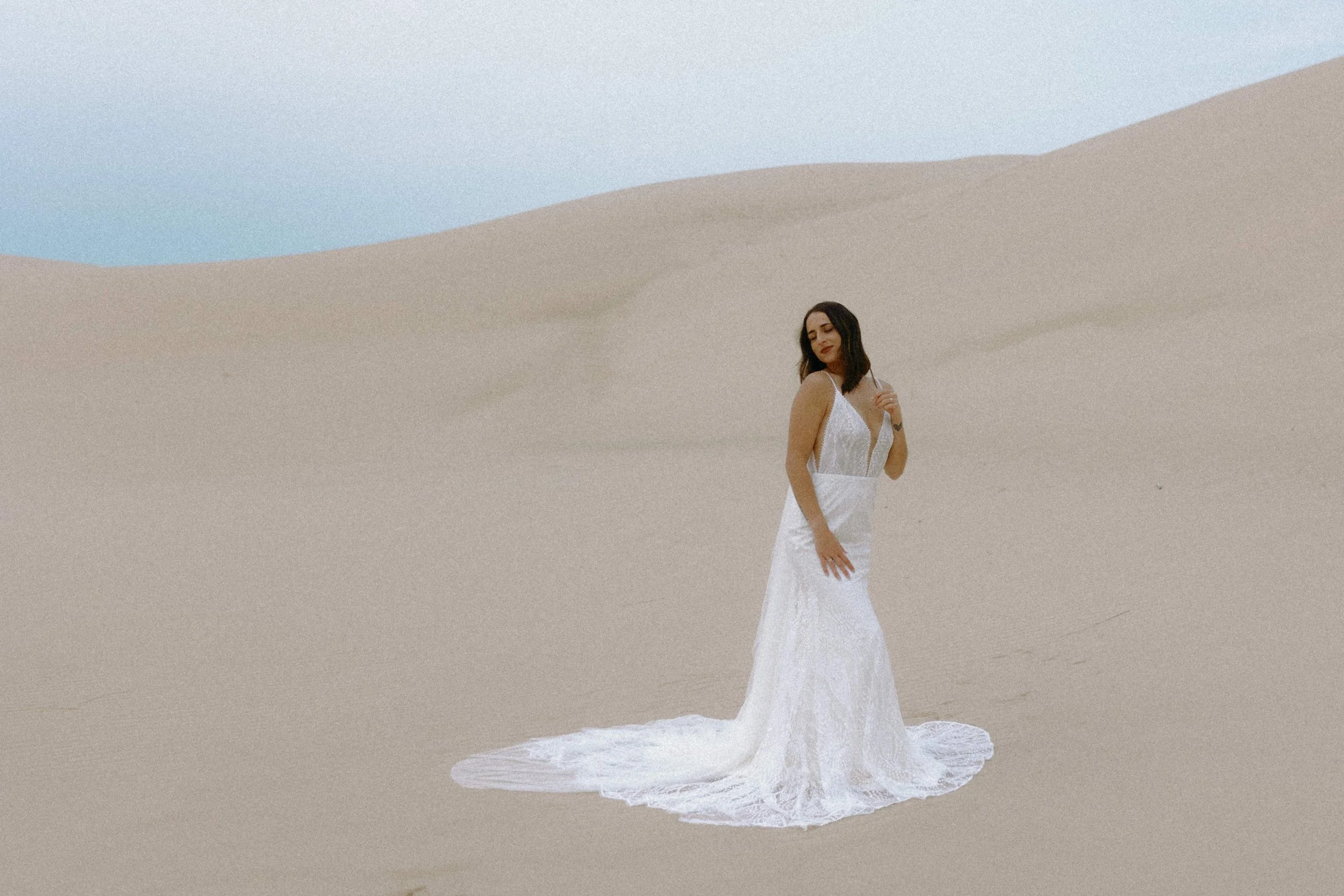 Bride in a white lace gown standing on the Silver Lake Sand Dunes in Michigan during an elopement photographed by Nicole Kilday