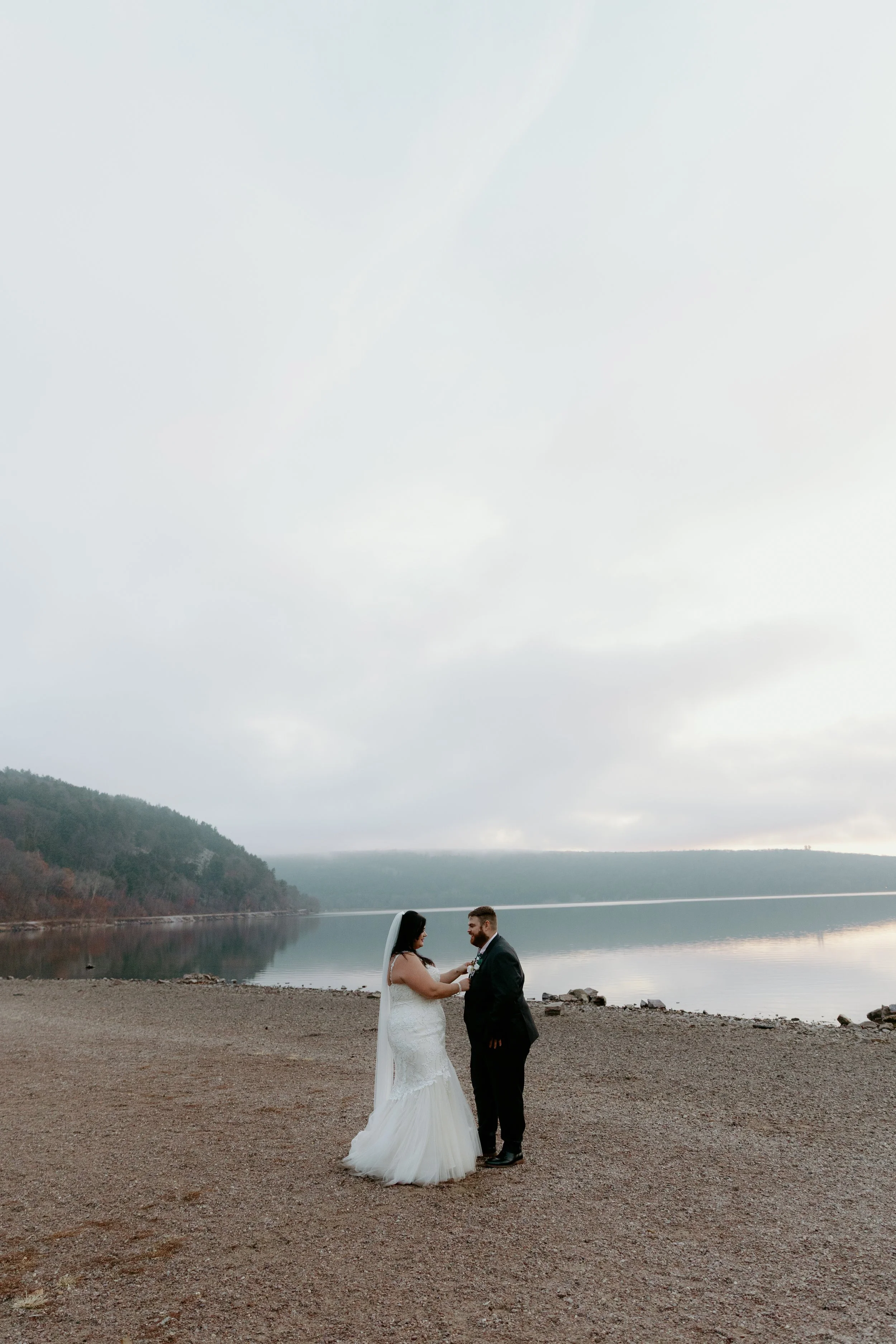 A bride and groom standing on the beach by Devil's Lake in Wisconsin with Devils Lake State Park in the background, exchanging wedding vows during overcast weather by Nicole Kilday Photography