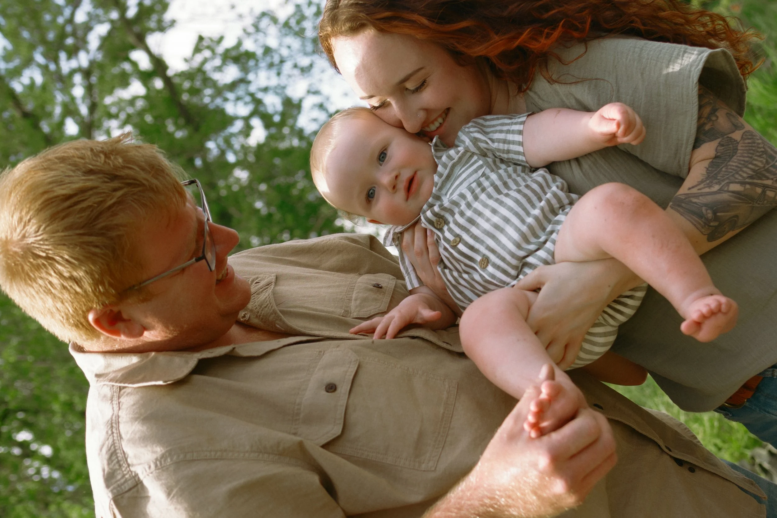 Candid motherhood and family photography moment with parents holding their baby outdoors during a relaxed milestone session in McHenry County, Illinois.