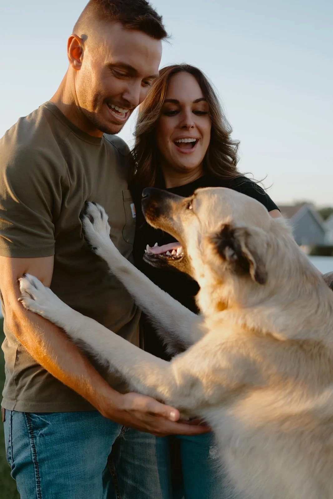 Nina and Matt laughing together at home in McHenry County, Illinois while petting their dog Hank during an at-home engagement session.