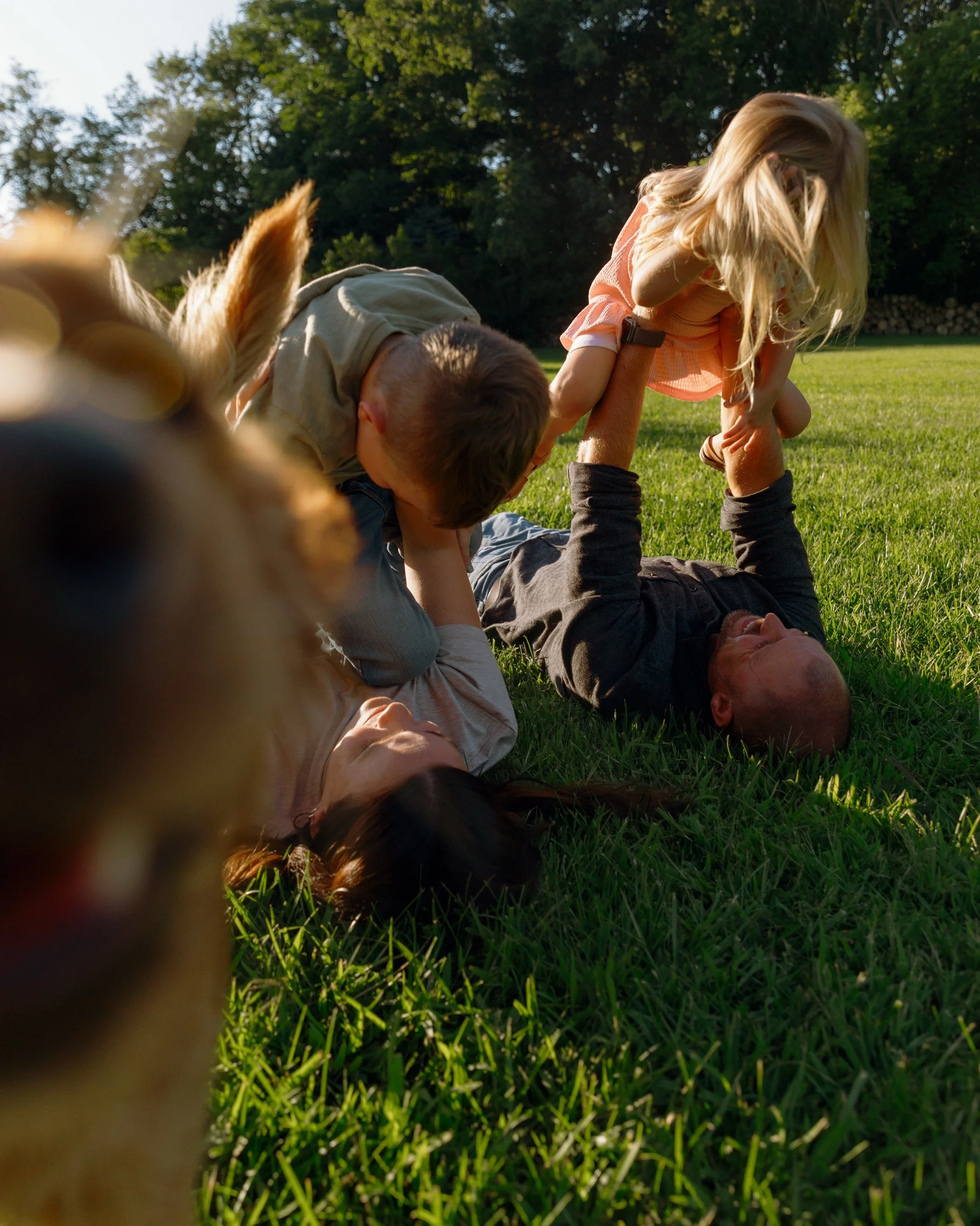 Little girl and boy playing on the grass with her parents and their golden retriever during an at-home family session in Twin Lakes, Wisconsin.
