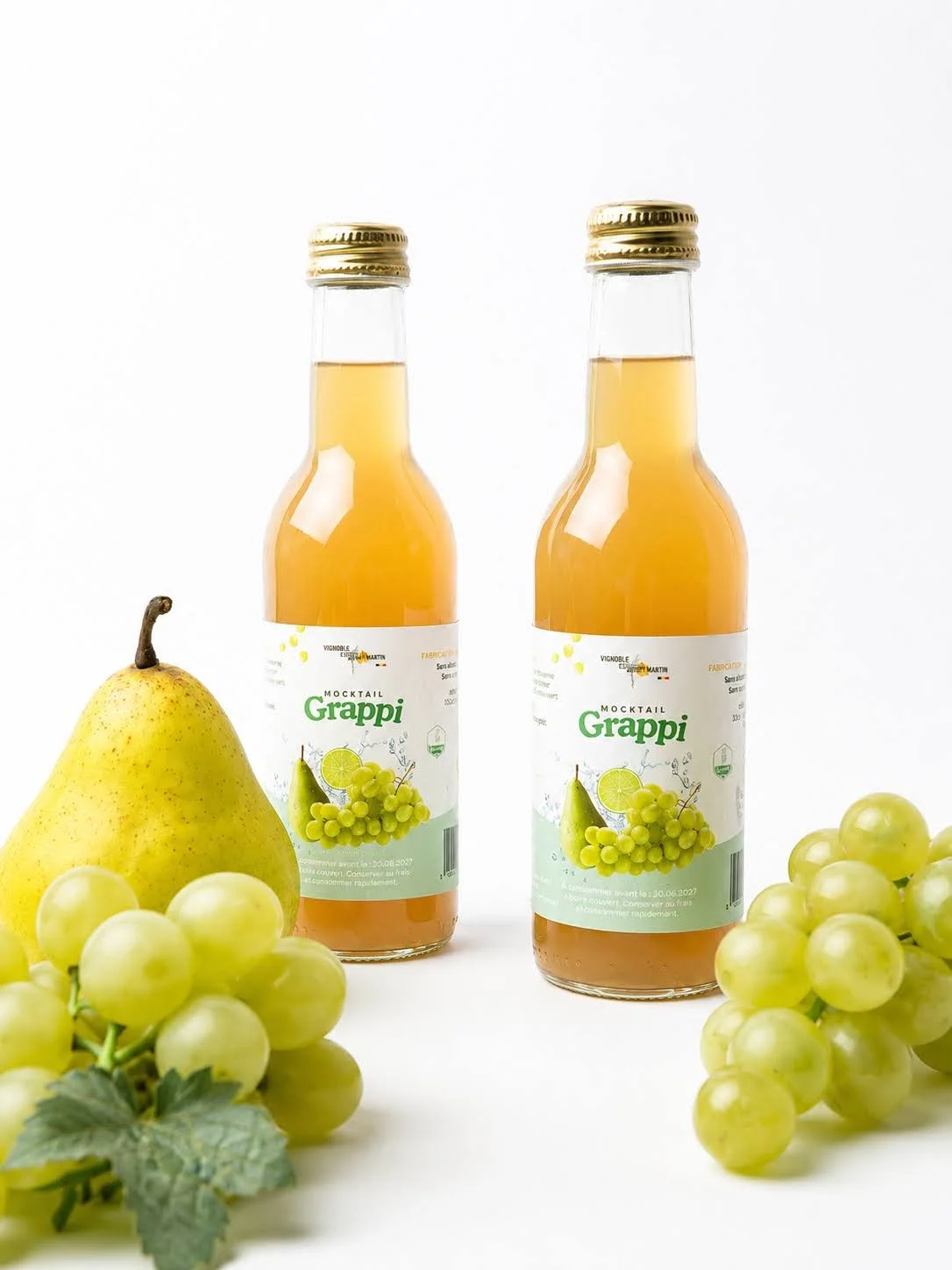 Deux bouteilles de mocktail Grappi au centre, entourées de raisins verts et une poire sur fond blanc.