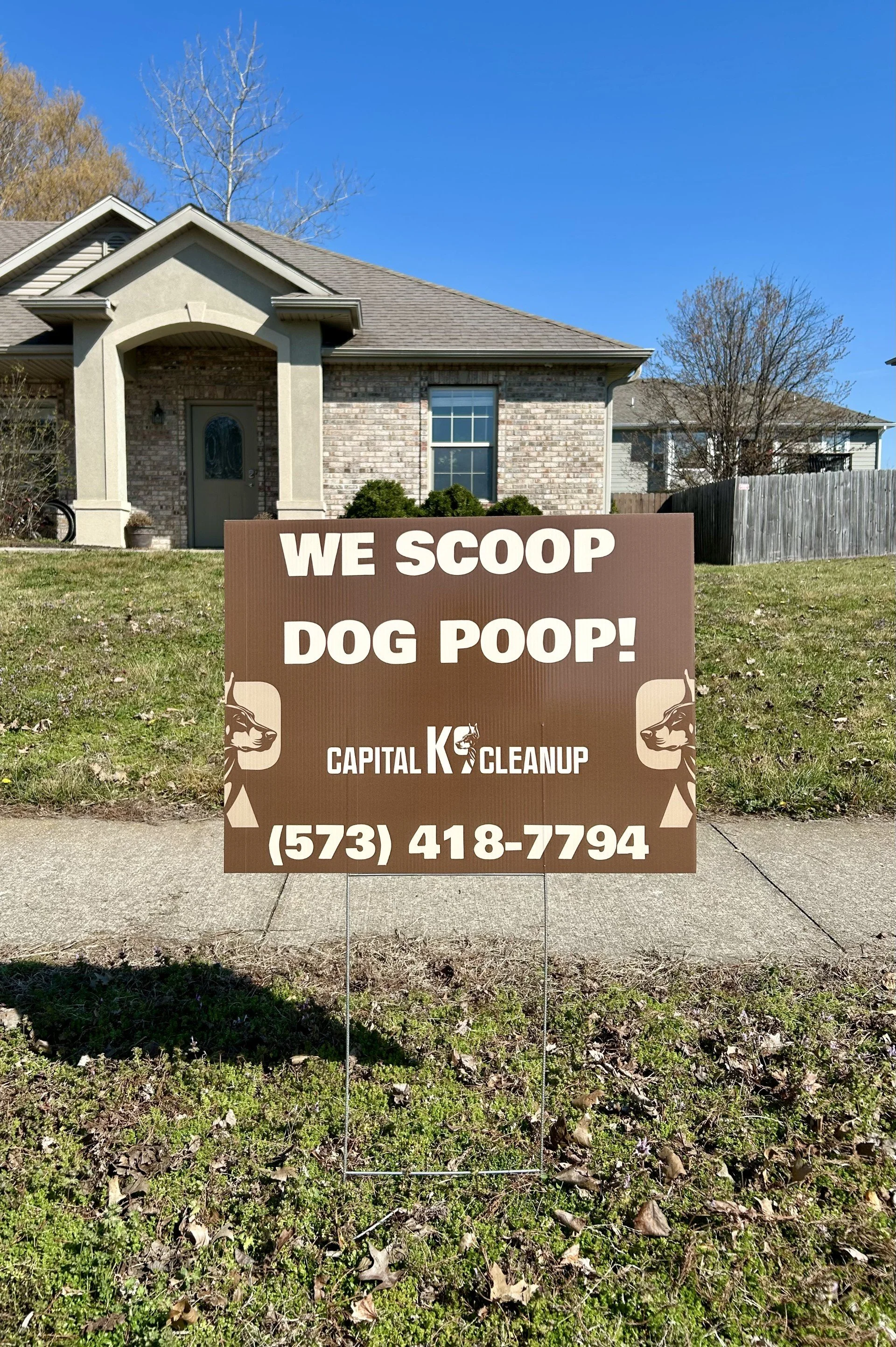 Sign in front of house advertises dog poop cleaning service with phone number.