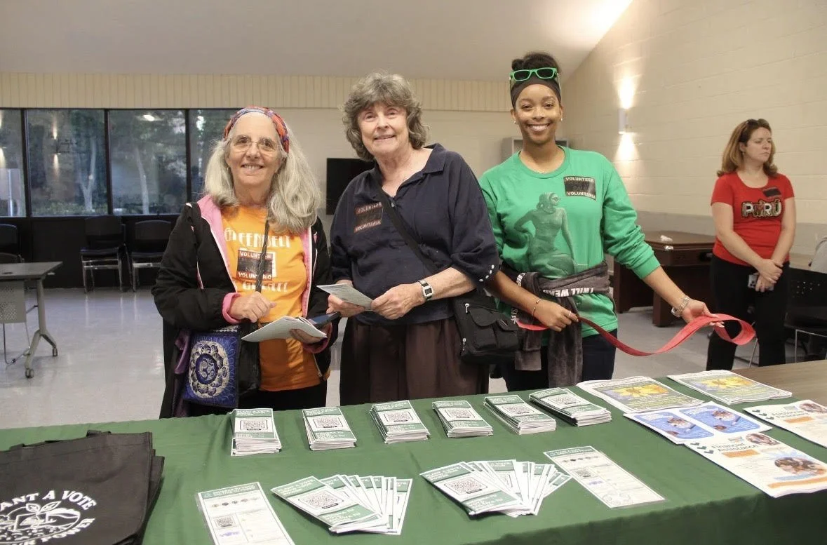 Shavonne and two volunteers smiling at a Salsa Y Salsa voter registration event standing at a table in front of pamphlets