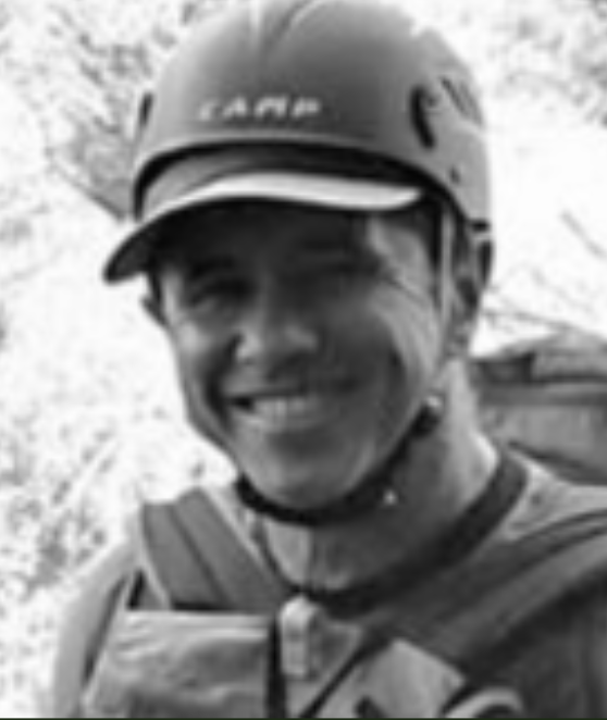 Pessoa sorrindo usando capacete de bicicleta, ao ar livre em um ambiente natural.