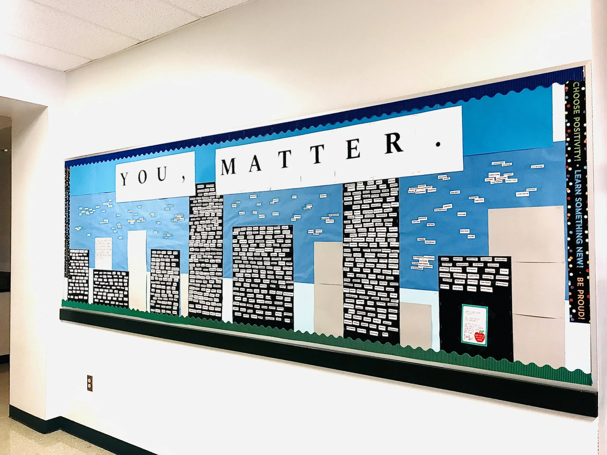 School bulletin board with the phrase 'You, Matter' and an illustrated city skyline with blue sky and clouds.