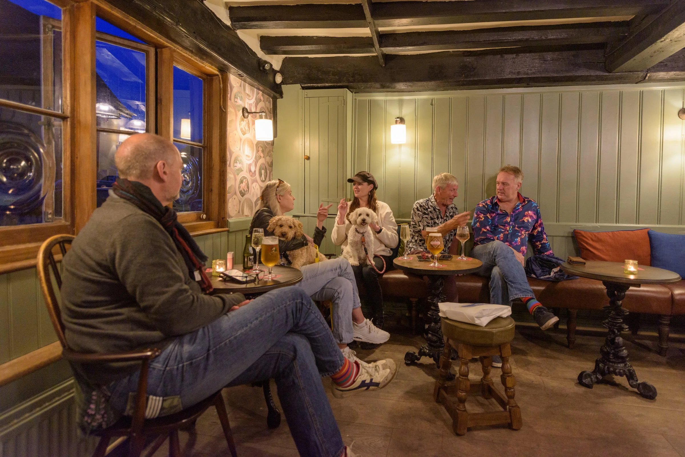 A group of guests enjoying drinks with their dogs inside a cosy pub setting, alongside seasonal dishes