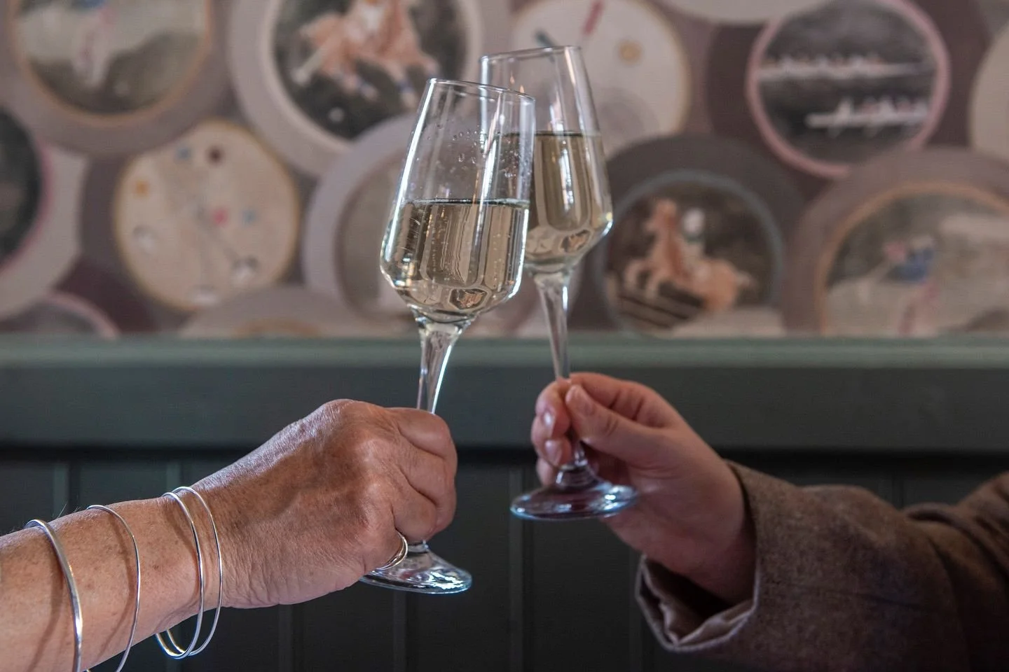 Two people raising glasses of sparkling wine in a toast during pub events, set against a decorative background inside a cosy venue