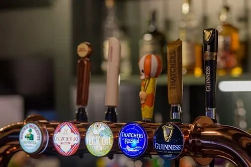 Beer taps serving a variety of popular drinks at a pub bar, perfect for lively pub events.
