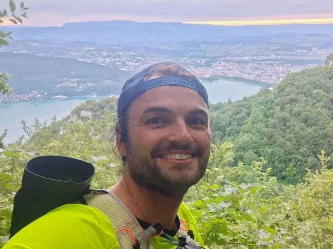 Homme souriant devant la vue du lac d'Annecy en tenue de trail