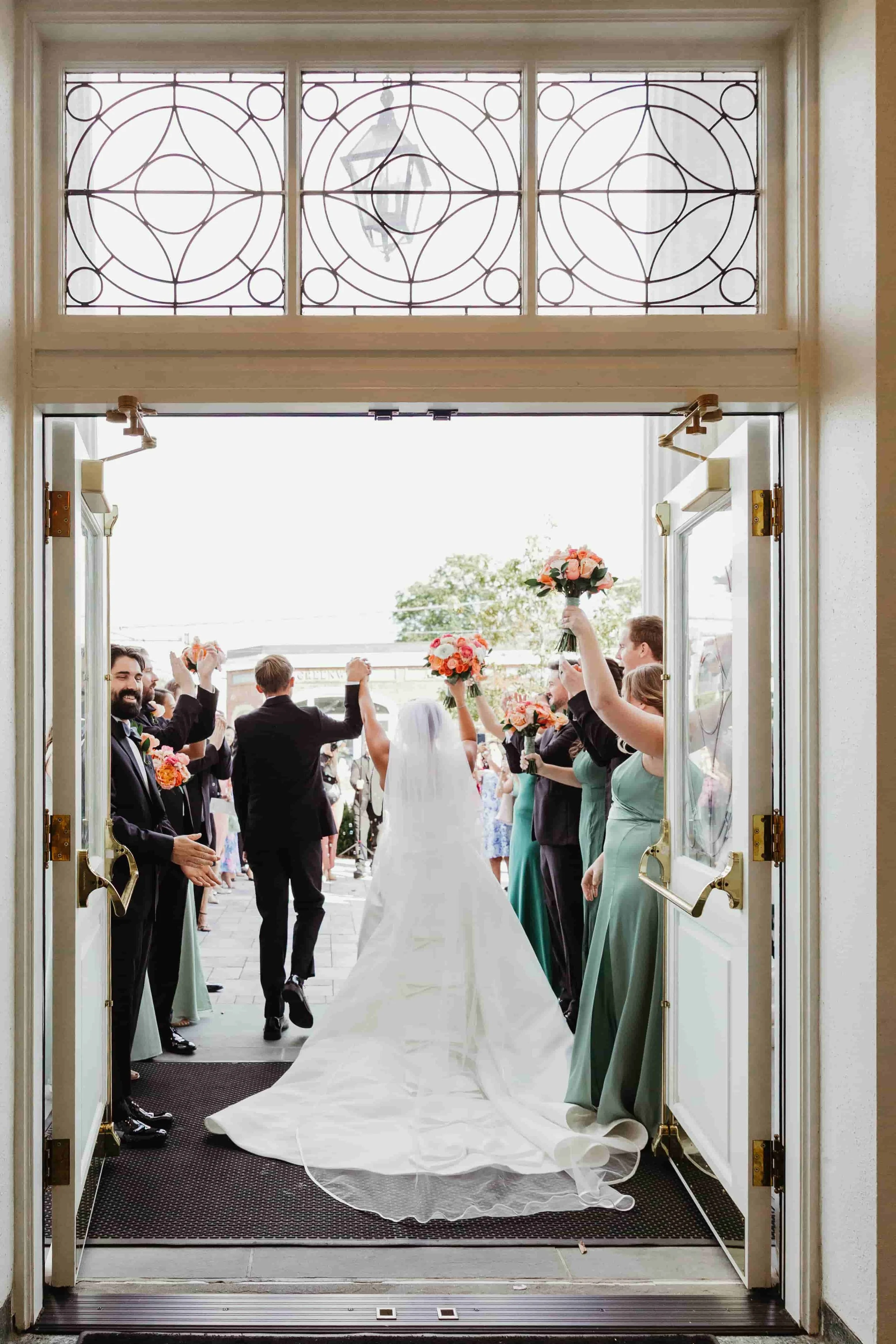Bride and groom walking out of church, wedding party and guests celebrating with bouquets and hand gestures outside in connecticut